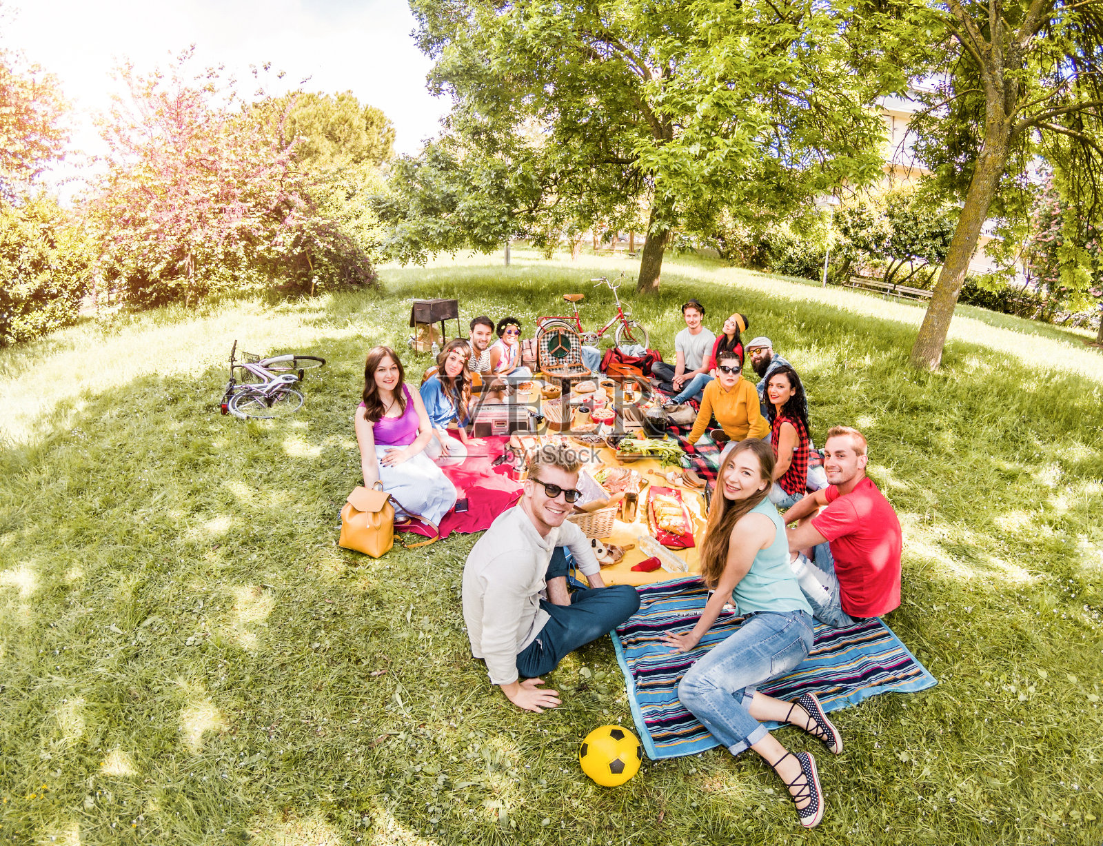 一群快乐的朋友在公共公园户外野餐-年轻人喝葡萄酒和在自然中欢笑-主要集中在底部的家伙-青春和友谊的概念-鱼眼镜头扭曲照片摄影图片