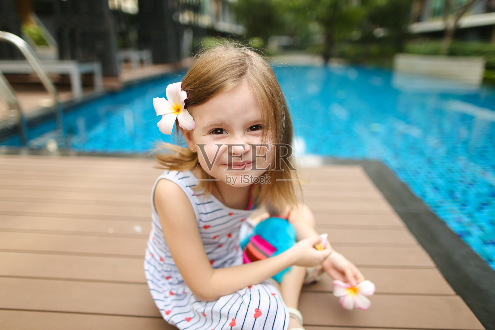 小女孩对着镜头微笑，坐在靠近游泳池的穿着照片摄影图片
