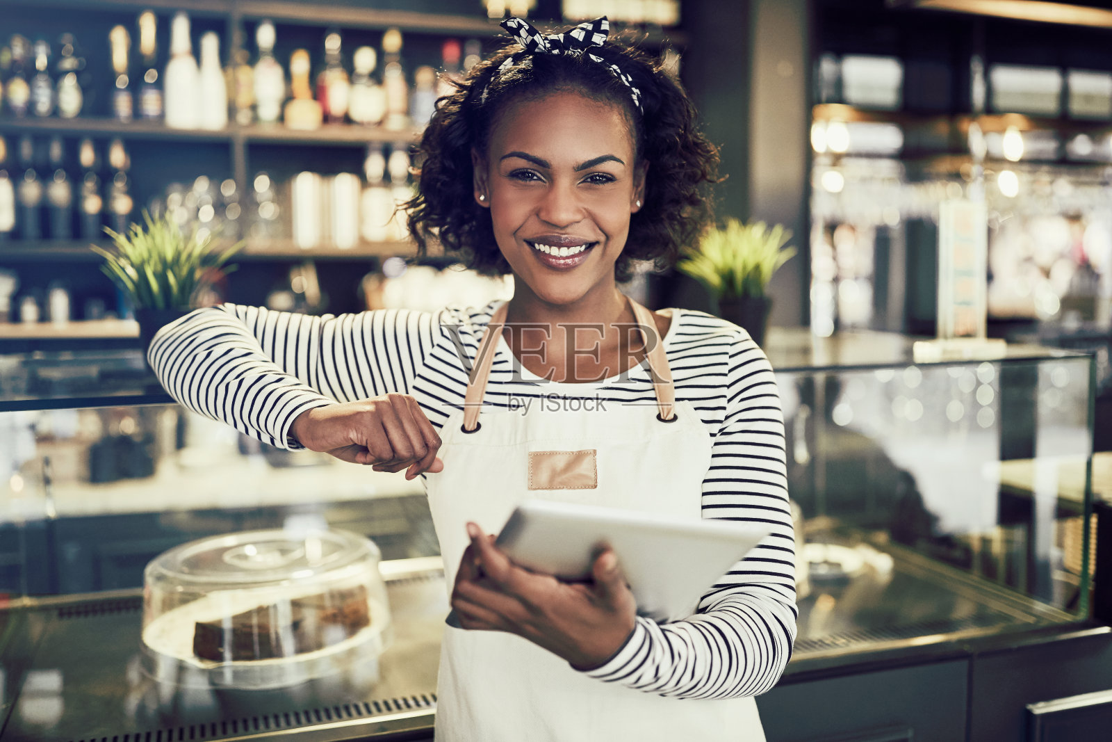 一位微笑的非洲企业家拿着平板电脑站在她的咖啡馆里照片摄影图片