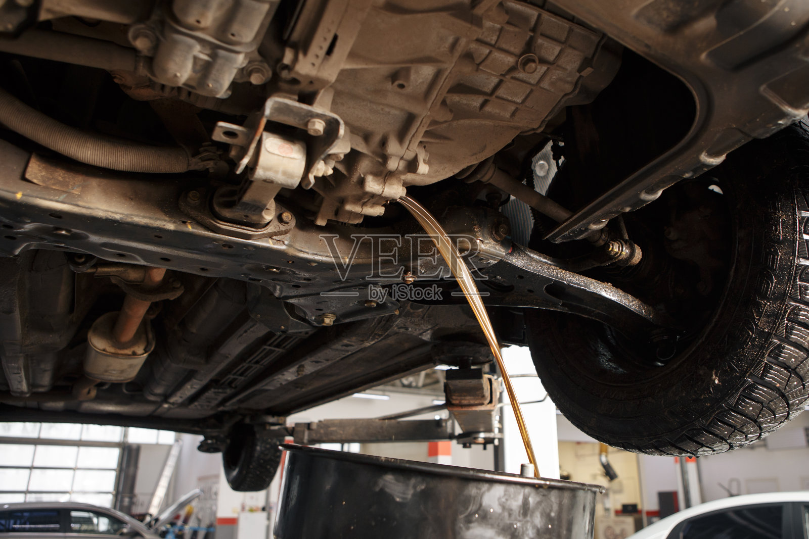 在汽车车间维修服务站为汽车发动机更换机油的专业汽车技师。照片摄影图片