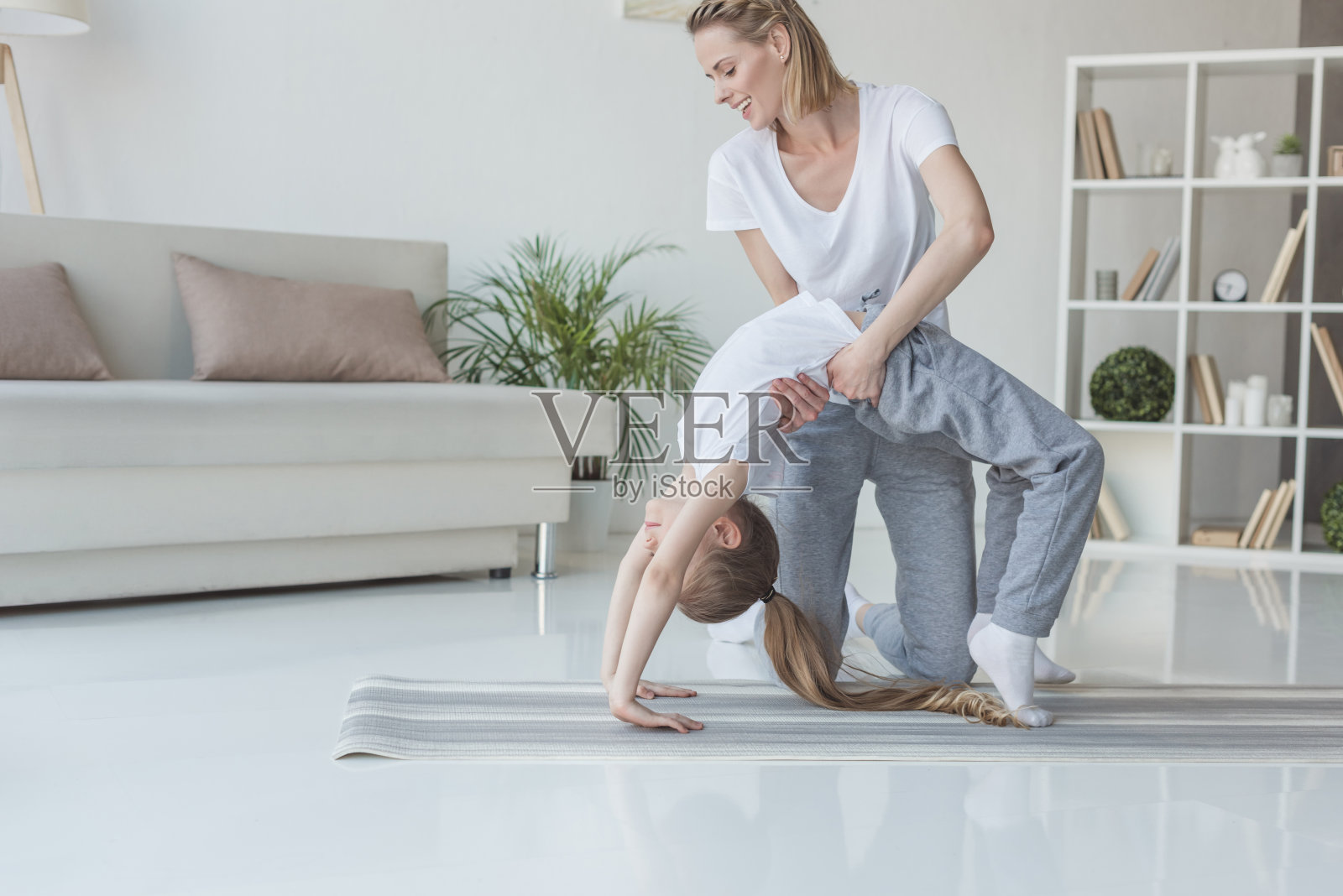 快乐的妈妈在家里教她的女儿站在瑜伽轮的姿势照片摄影图片