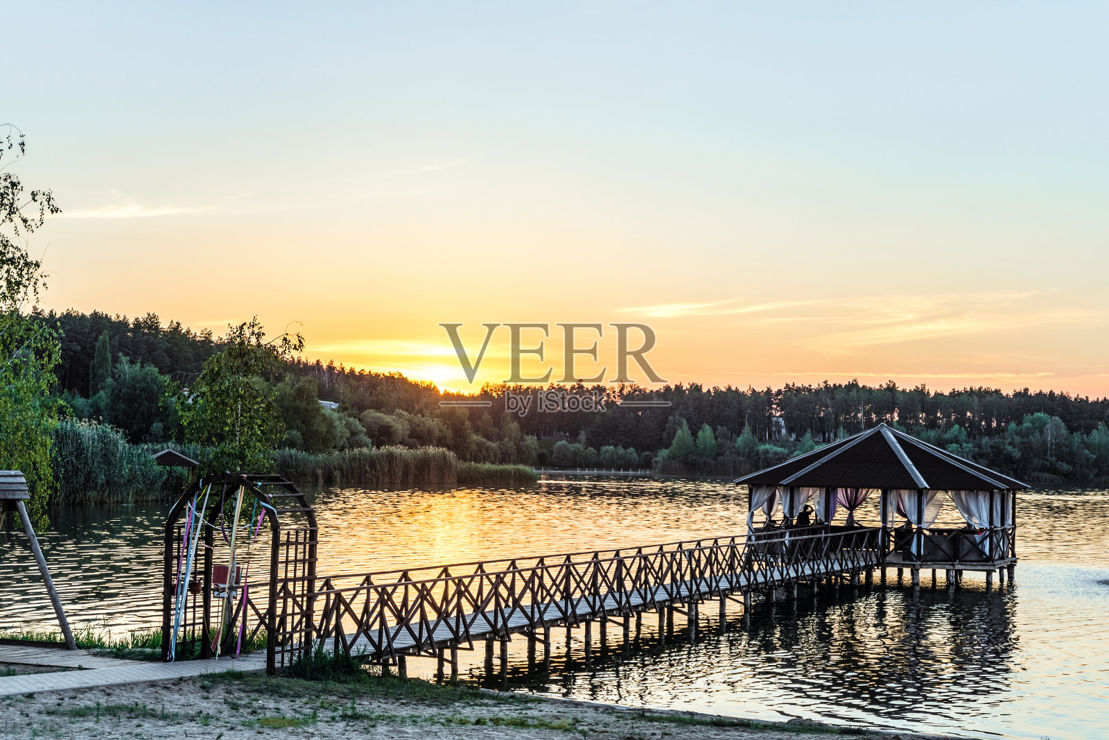 在夕阳的照耀下，湖边有一个凉亭的人行桥。日落和宁静的假期在大自然中。照片摄影图片