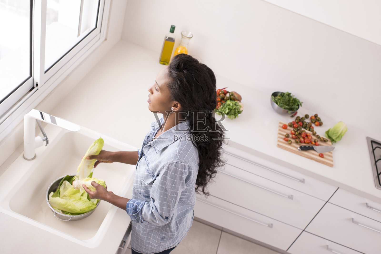 高角度的女人在厨房冲洗生菜。照片摄影图片