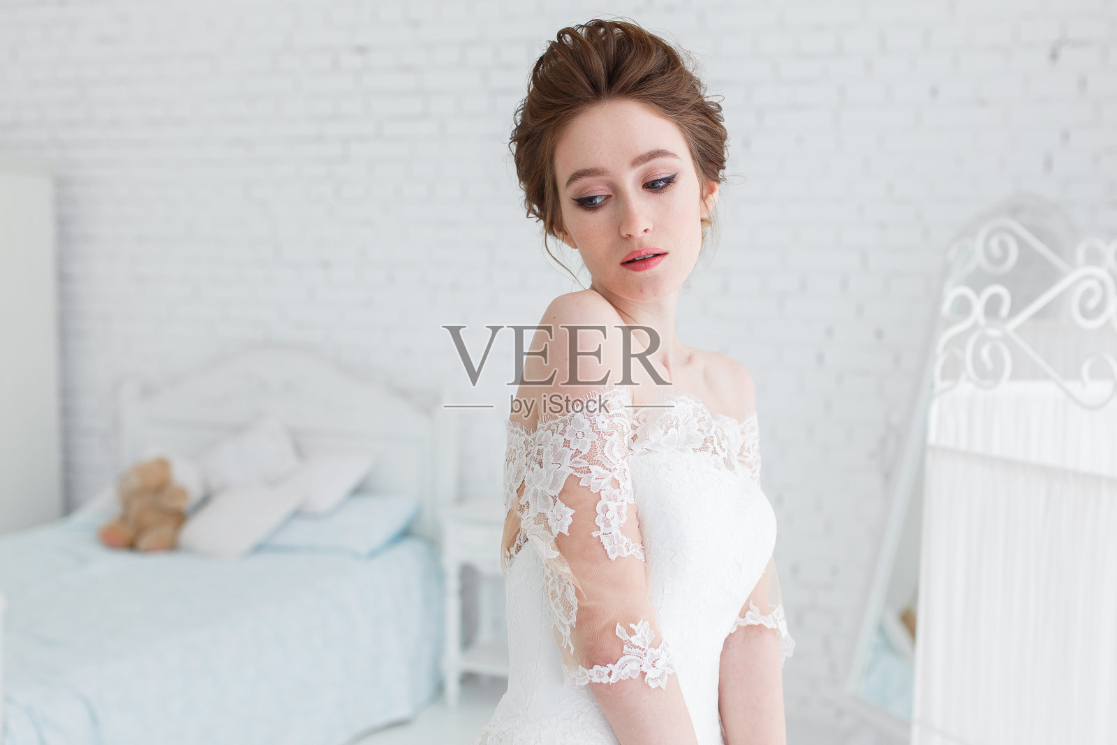 新娘穿着婚纱在工作室里摆姿势，背景是砖墙和白色的床。水平接近的肖像照片摄影图片