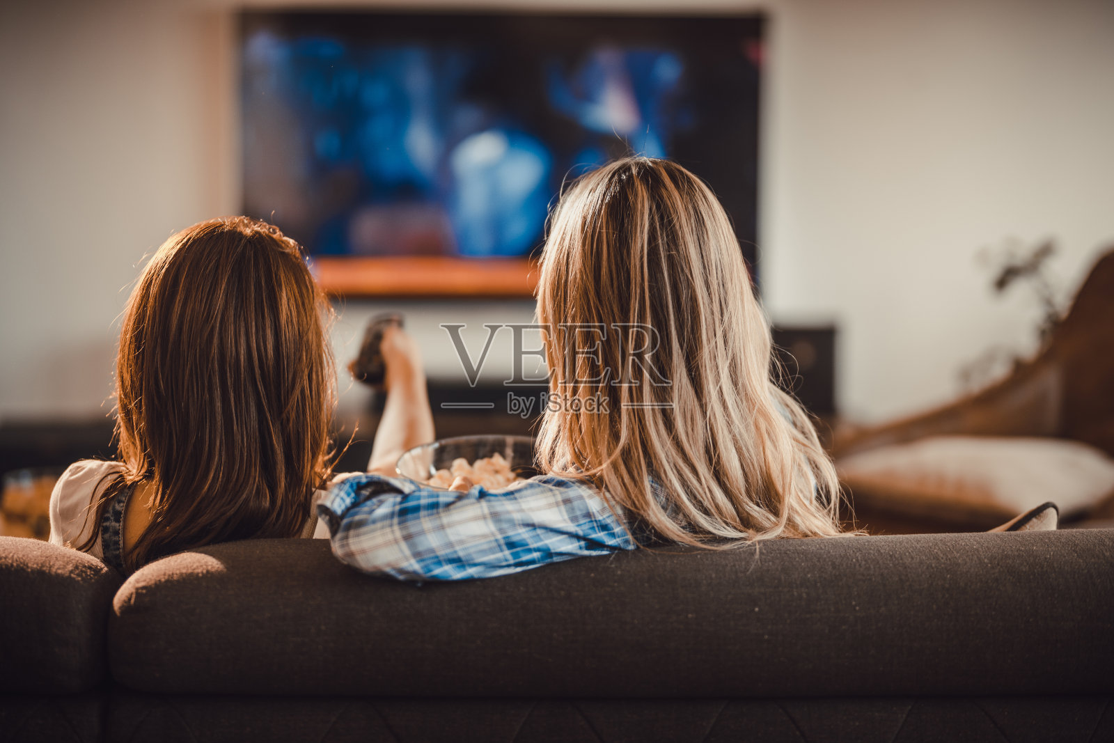 后视图两个女人放松在沙发上的客厅和看电视上的电影。照片摄影图片