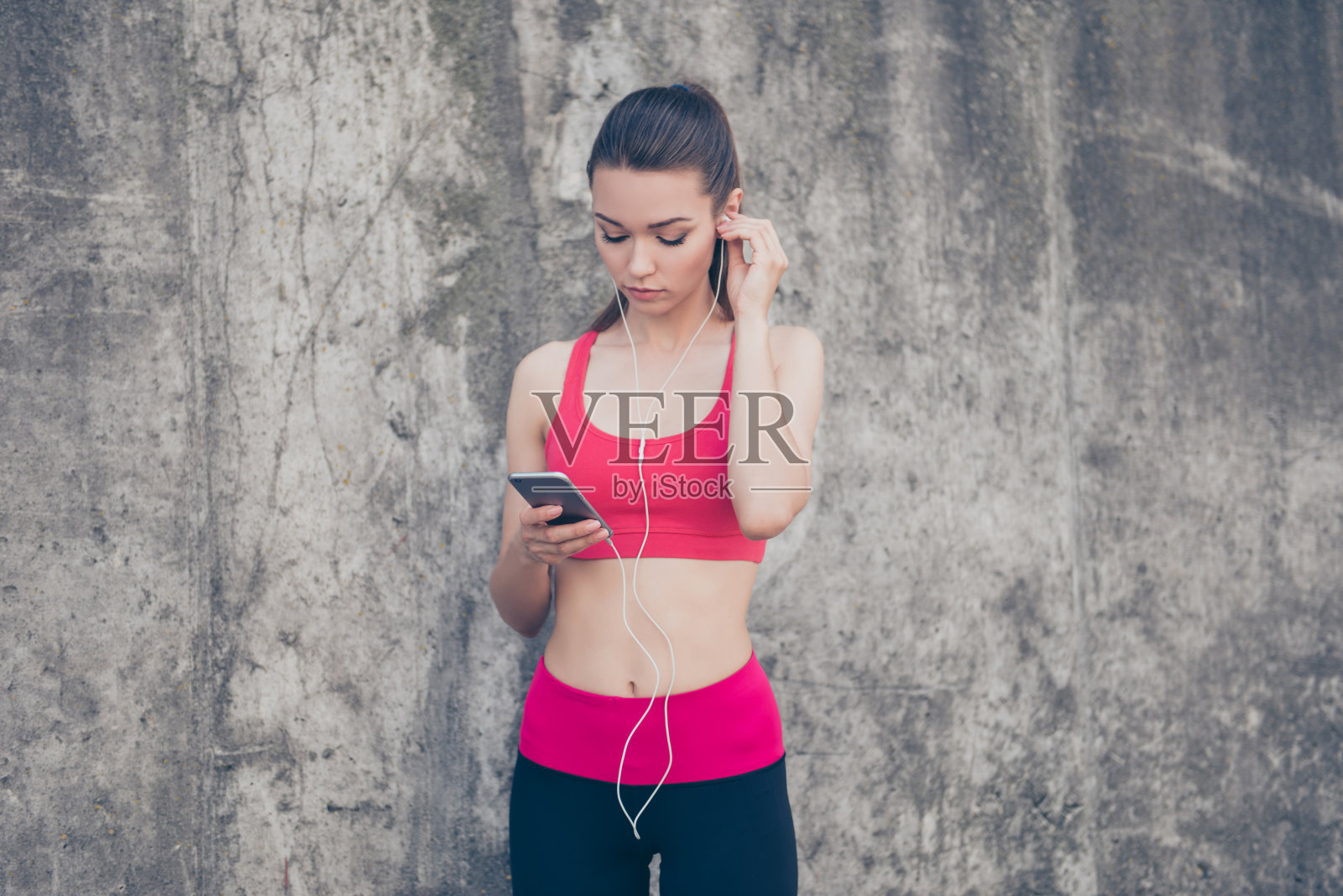 迷人的健身女运动员在锻炼前在智能手机上放音乐。她在夏天的户外，穿着时髦的运动服照片摄影图片
