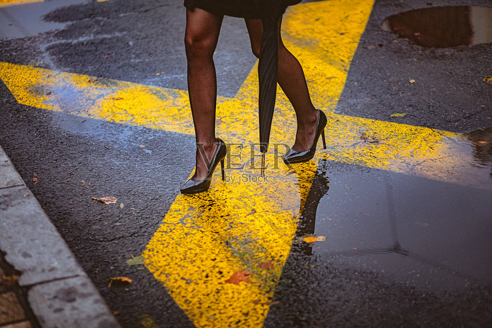 低段优雅的女人穿着高跟鞋走在潮湿的城市街道上照片摄影图片