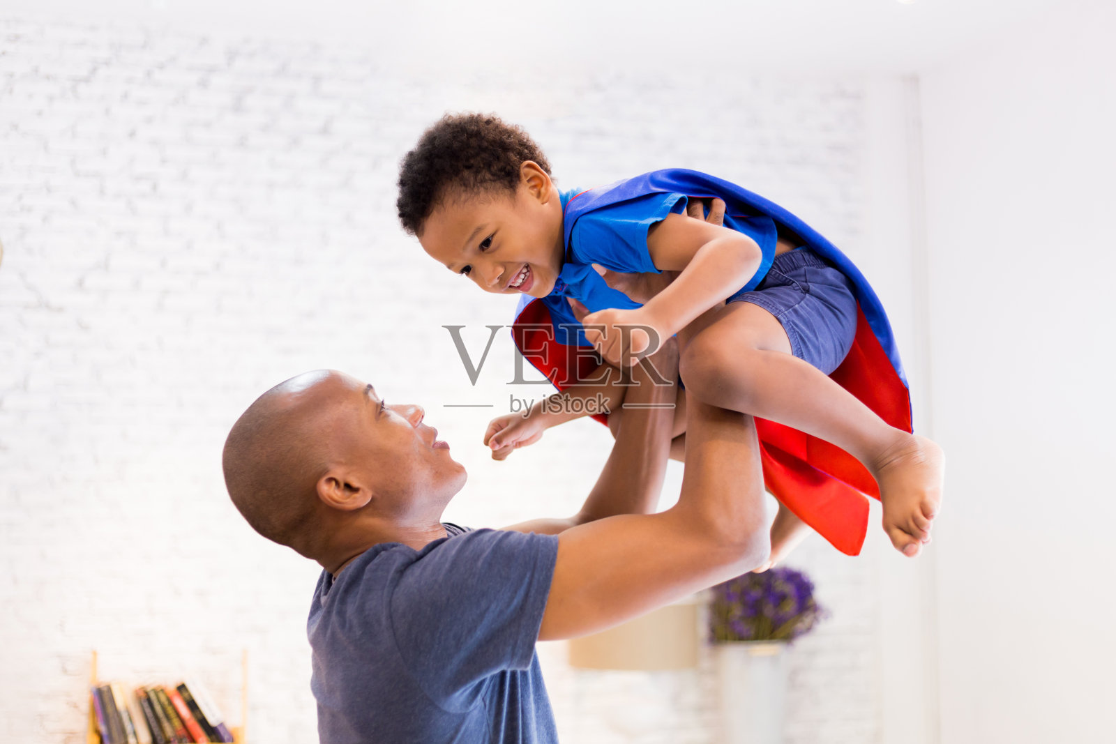 父亲抱着儿子，穿着超级英雄服装在家照片摄影图片