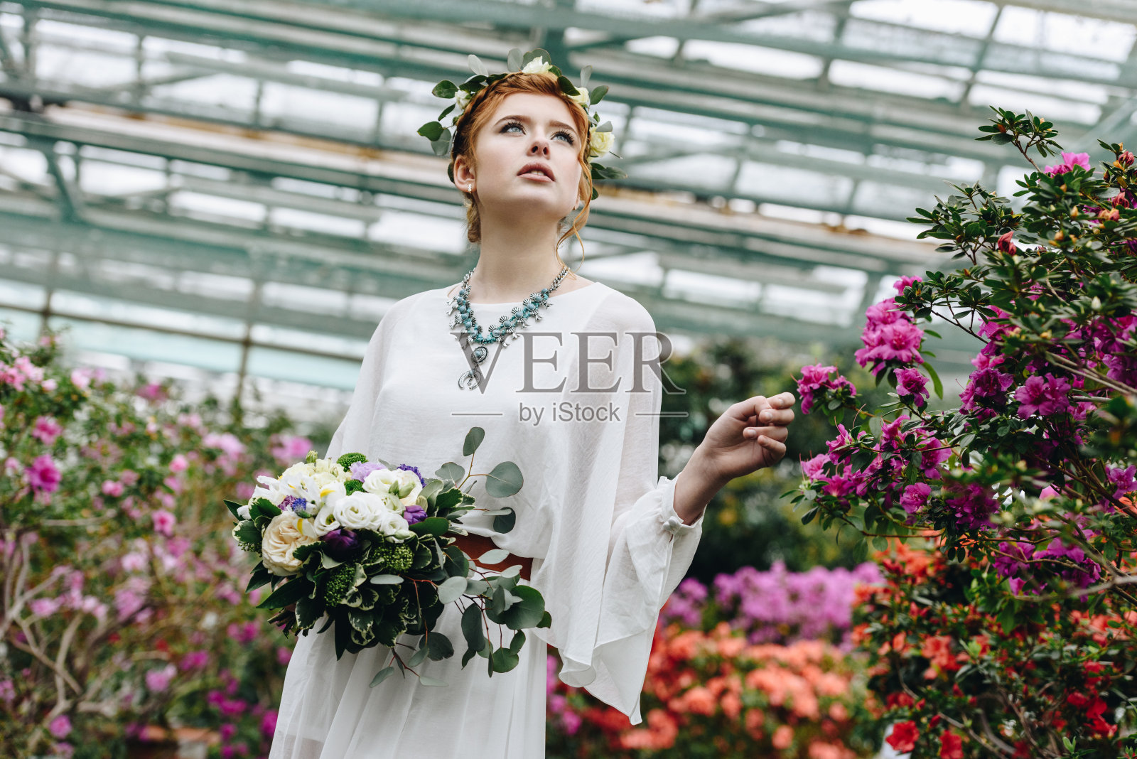 美丽的年轻女子在植物园穿着白色的礼服和手持婚礼花束的花圈照片摄影图片