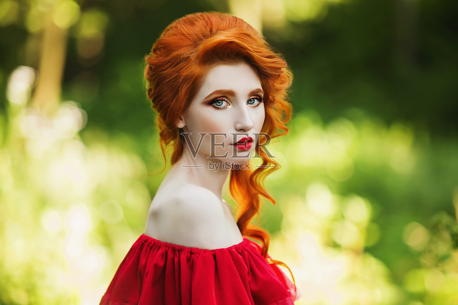 美丽的红发女孩在绿色的背景下摆姿势。夏日森林里一个红头发女人的肖像照片摄影图片