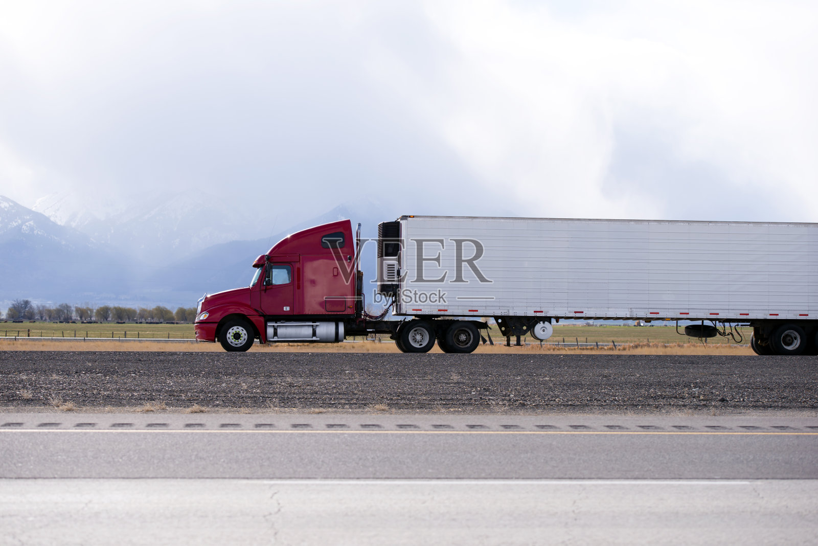 红色的大卡车装载着制冷半挂车，在犹他州的平坦道路上行驶照片摄影图片