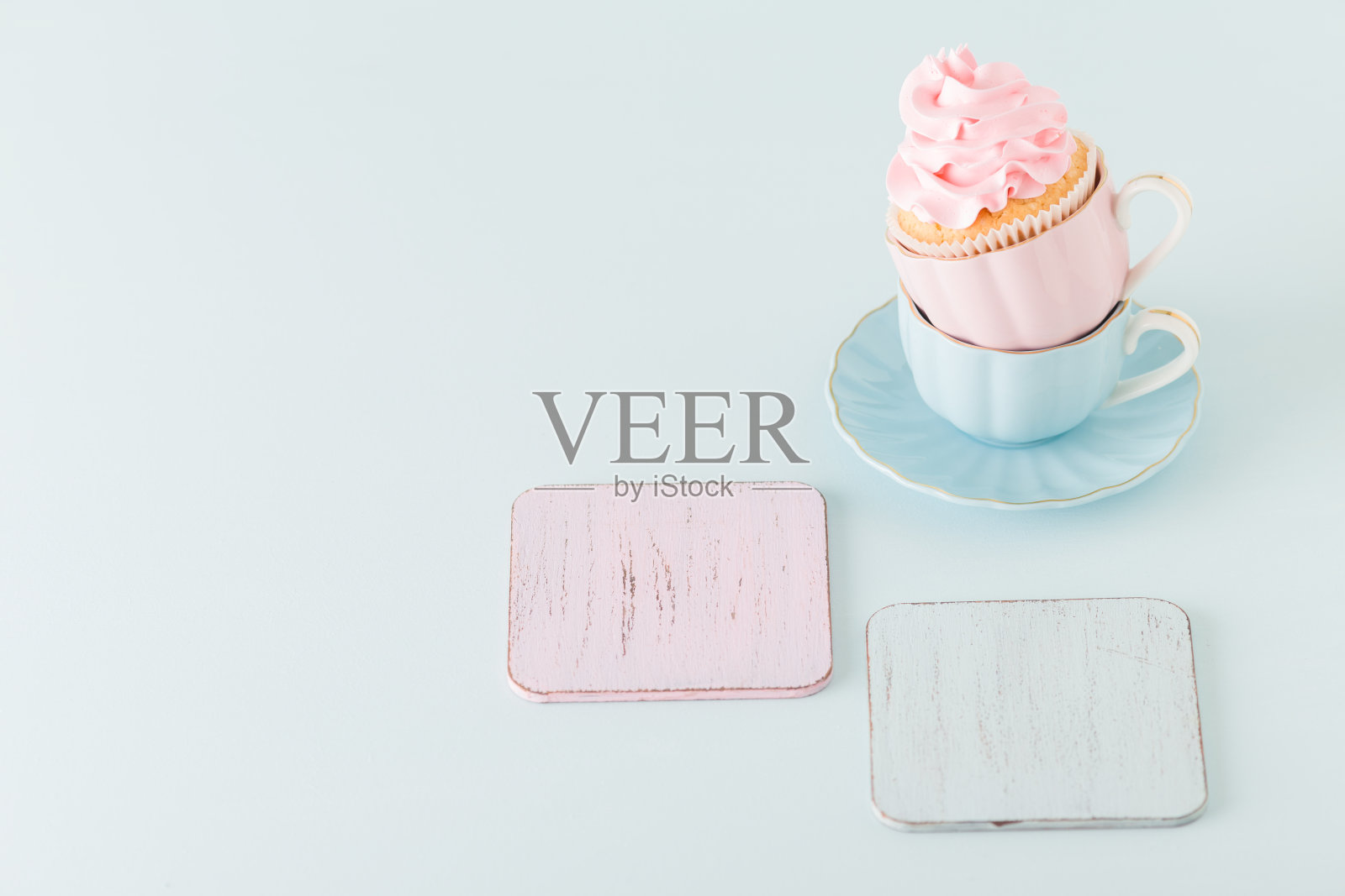 杯形蛋糕，两个杯子上有柔和的粉色奶油装饰，蓝色背景。照片摄影图片