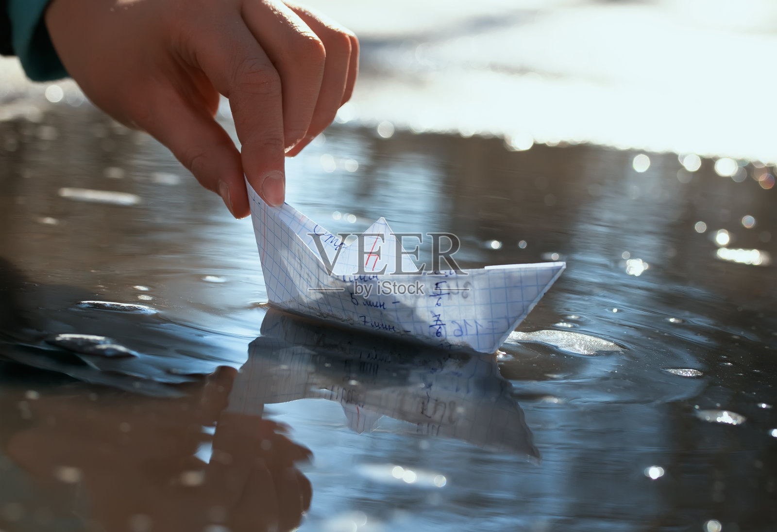 在一个阳光明媚的日子里，一个小学生的手在一个早春的水坑里用一个学校的笔记本做了一个小纸船照片摄影图片