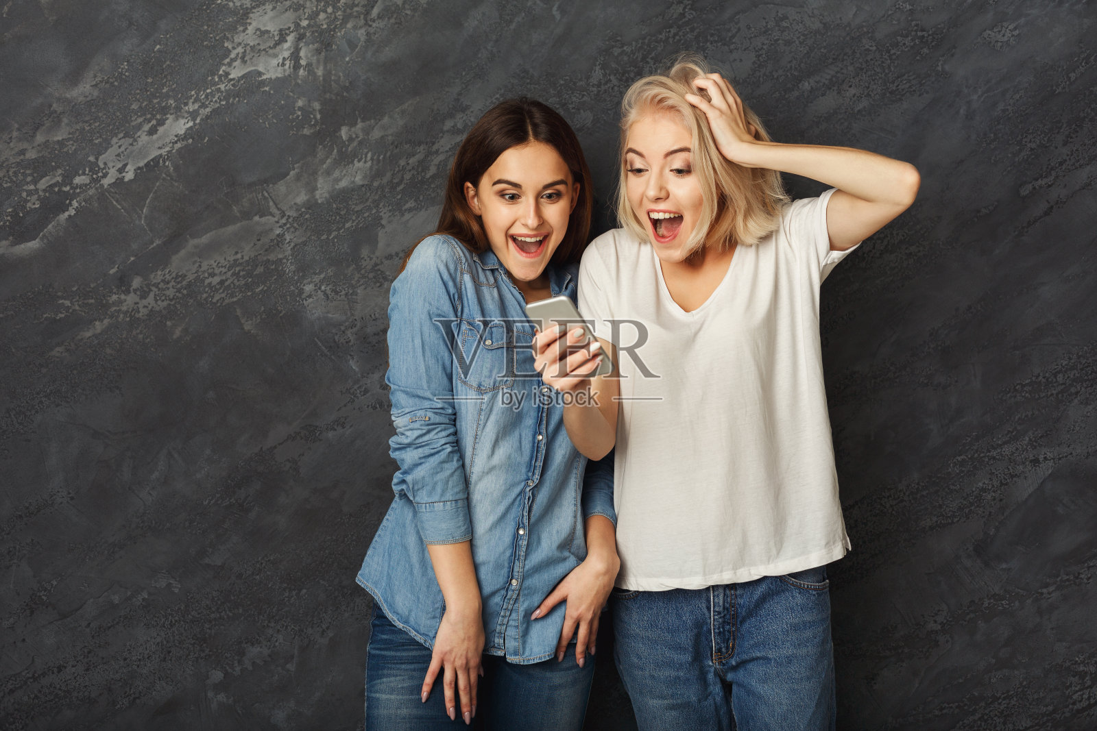惊讶的女性朋友在黑暗的工作室背景下使用智能手机照片摄影图片