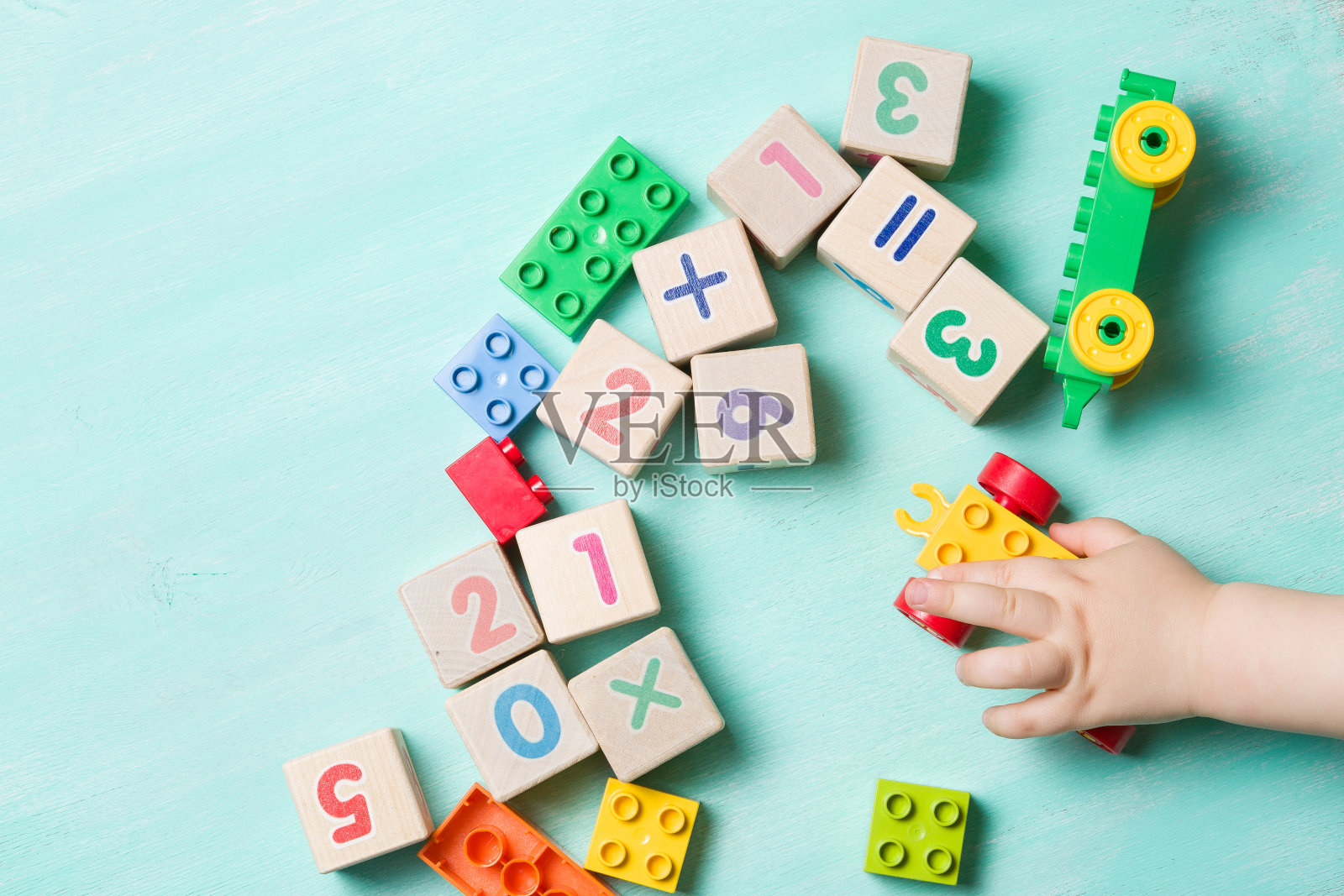 孩子们在绿松石木制的背景上玩有数字和彩色玩具积木的木立方体。幼儿学习数字。拿玩具的孩子的手。照片摄影图片