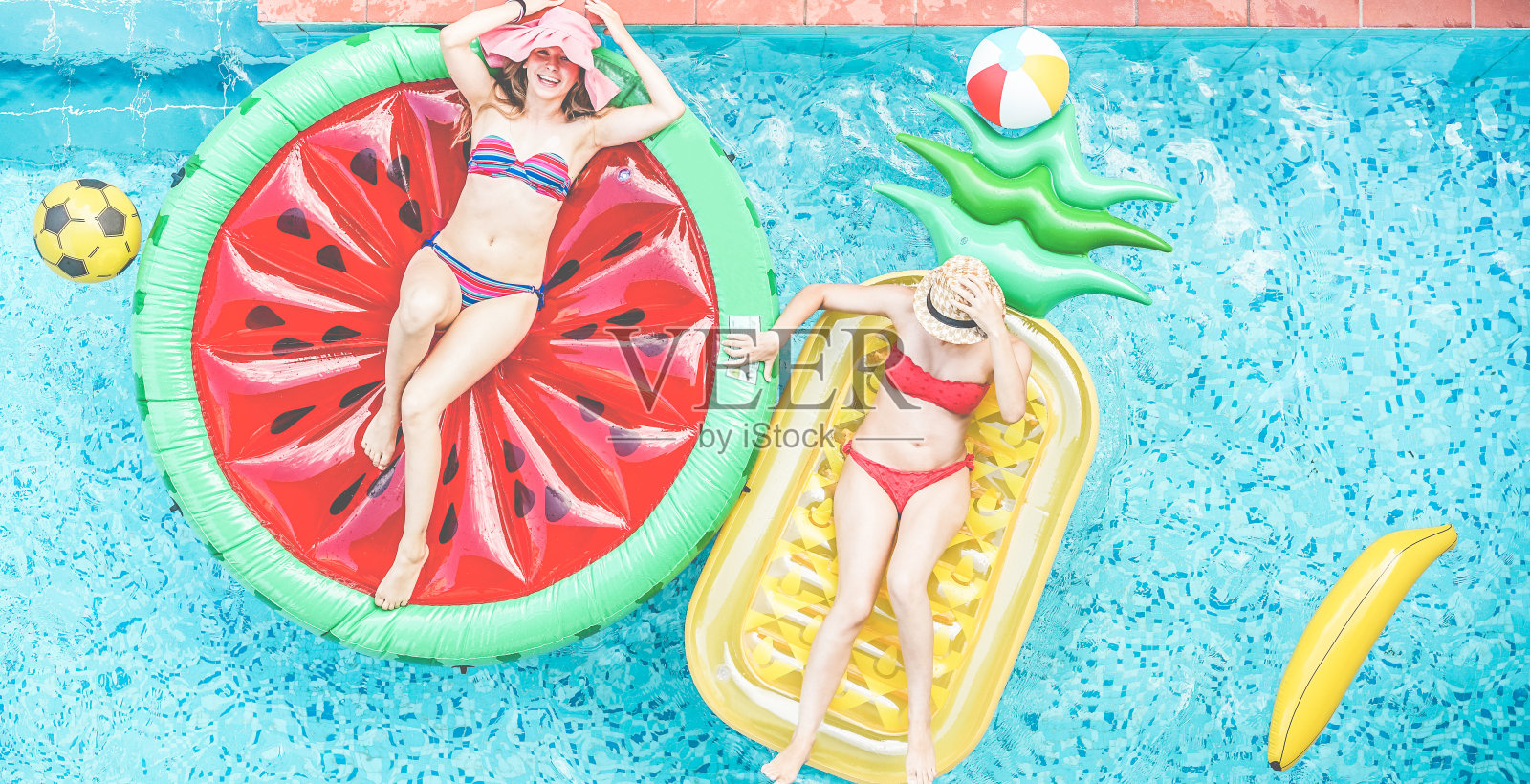 快乐的女孩漂浮在游泳池里热带水果lilos -年轻的女性朋友放松在度假酒店的暑假-旅游，寒冷，假期，青年概念-关注帽子照片摄影图片