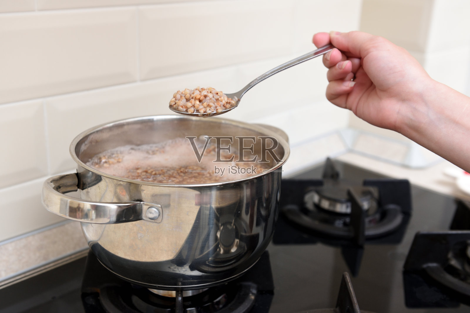 女孩的手握着炖锅上的勺子煮熟的荞麦照片摄影图片
