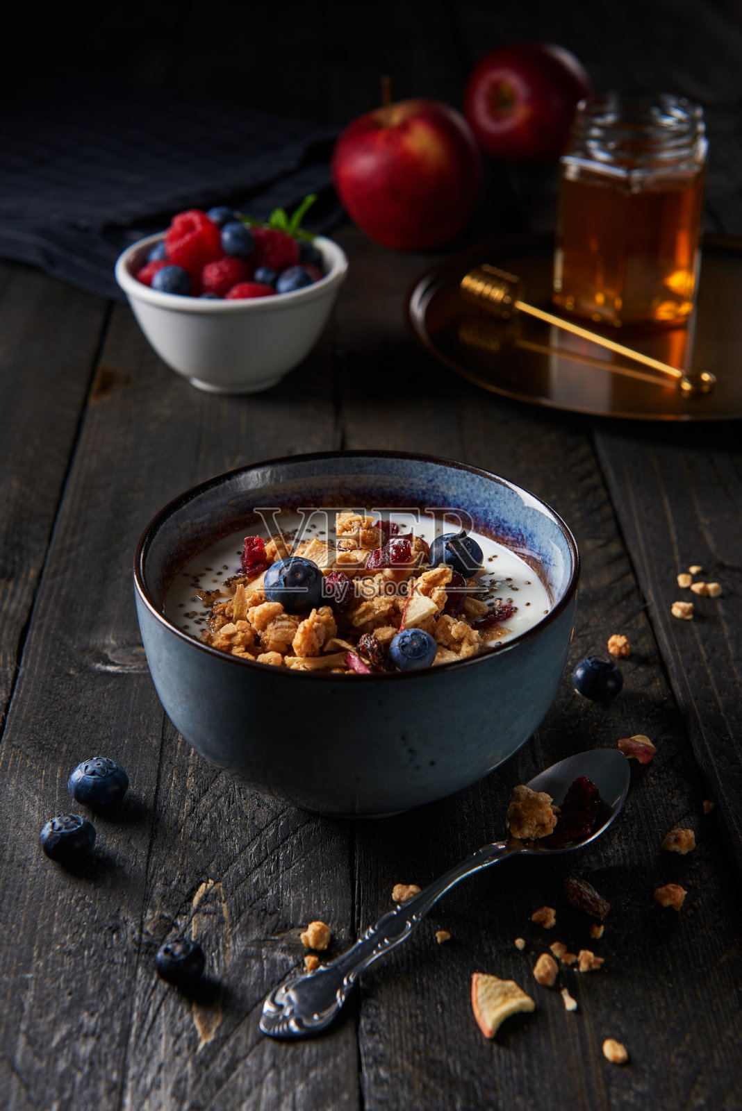 健康的早餐。新鲜的格兰诺拉麦片，酸奶，蓝莓，苹果干和蔓越莓，奇亚籽和枫糖浆在深色的木材背景。照片摄影图片