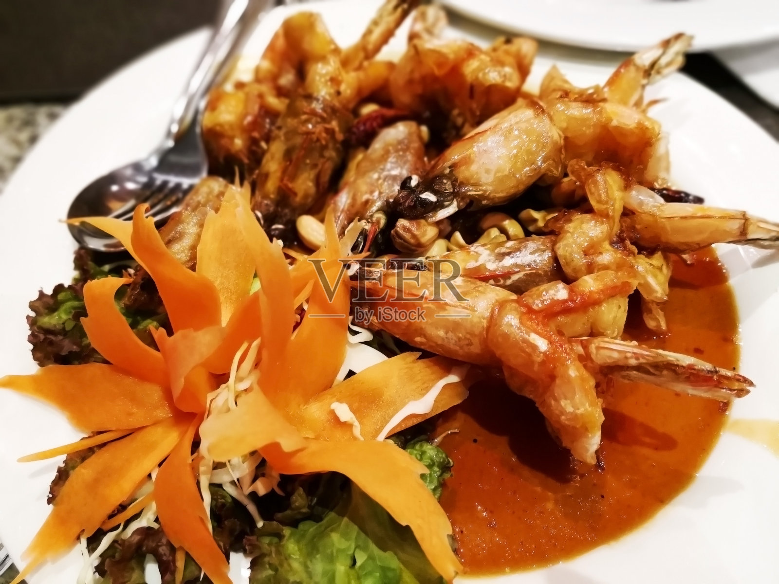 泰国菜的概念。白盘子上的罗望子酱虾仁。味道是辛辣、酸甜的。这道菜用绿橡木、红橡木、切成薄片的卷心菜和胡萝卜来装饰。专注于前景。照片摄影图片