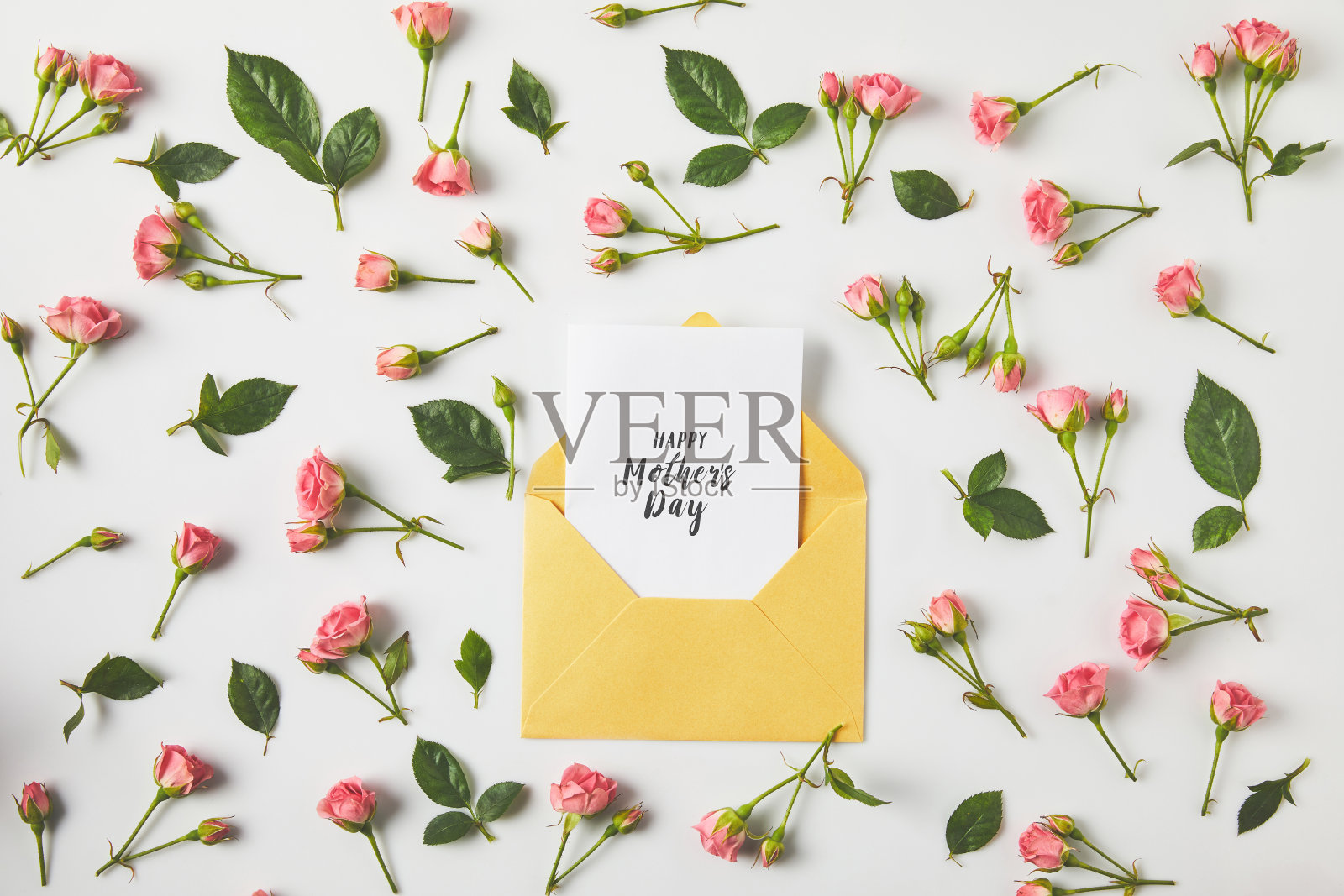 母亲节快乐贺卡装在信封里，美丽的粉红色玫瑰和绿色的叶子在灰色照片摄影图片