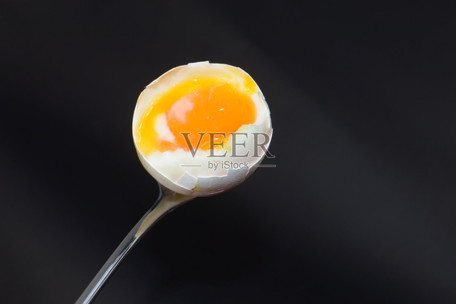 黑色背景下，银勺子上一个打开的鸡蛋照片摄影图片