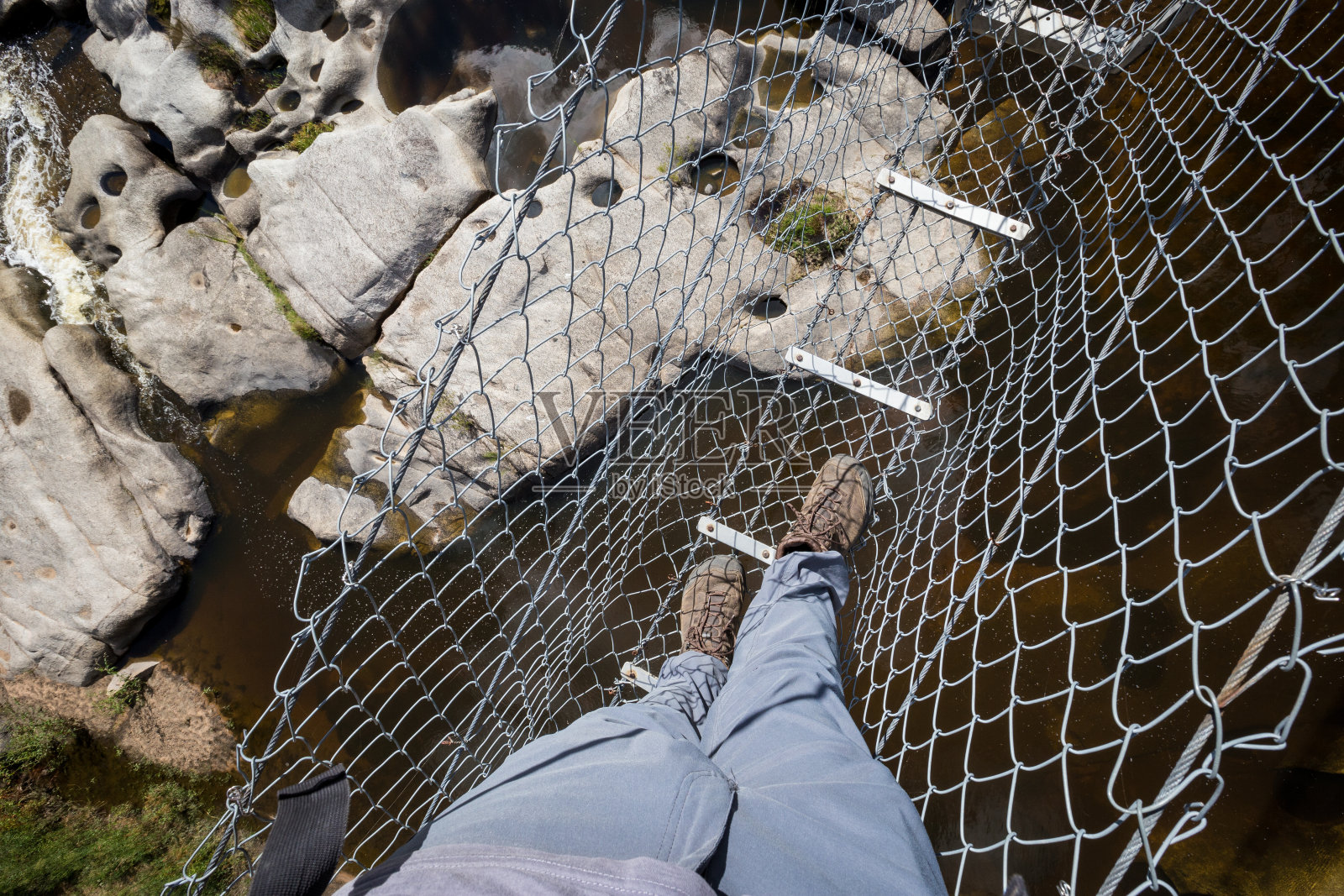 一个穿着灰色裤子的徒步旅行者穿过河上岩石上的吊桥的观点照片摄影图片