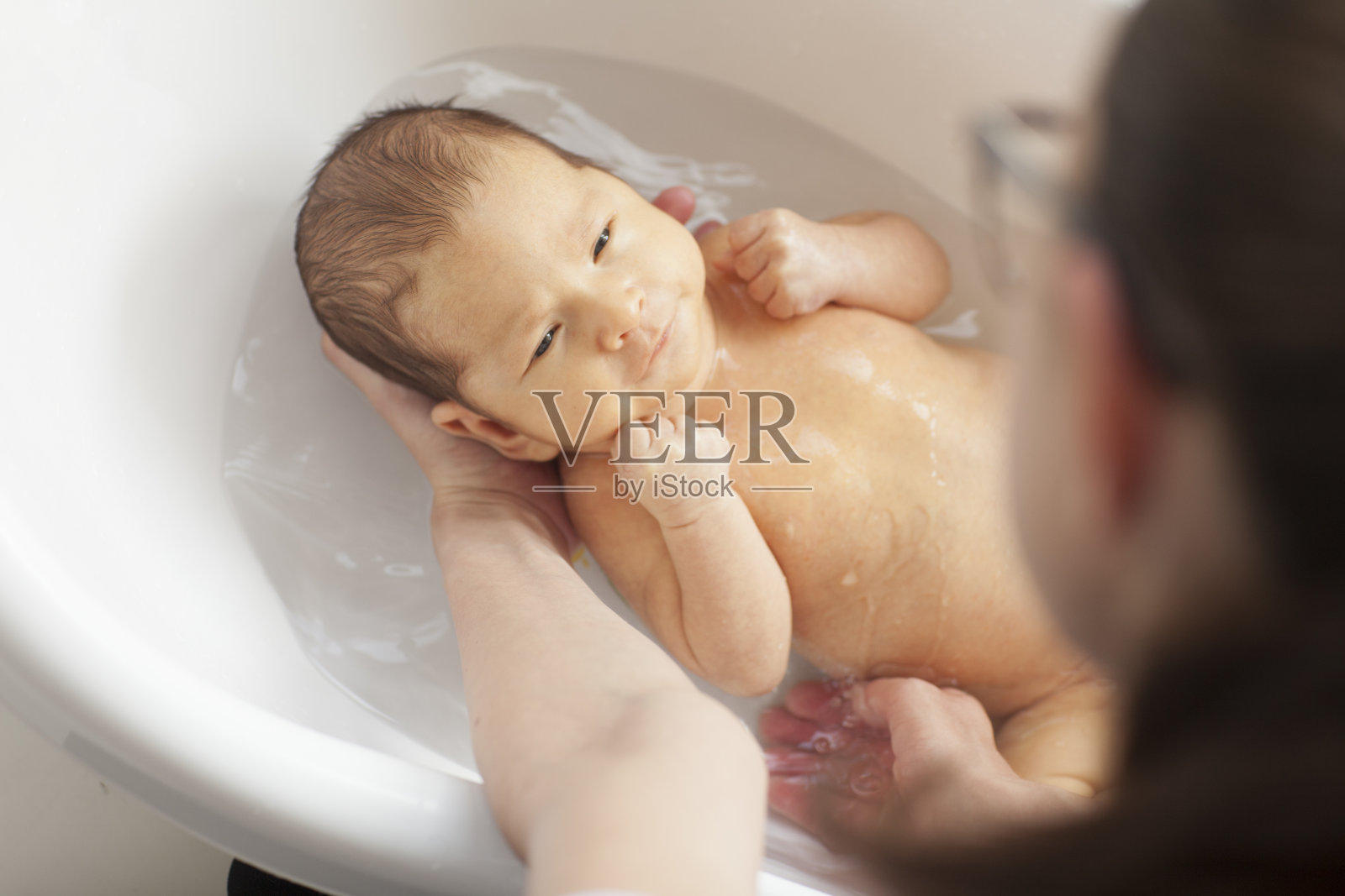 小婴儿在她妈妈的臂弯里洗澡。照片摄影图片