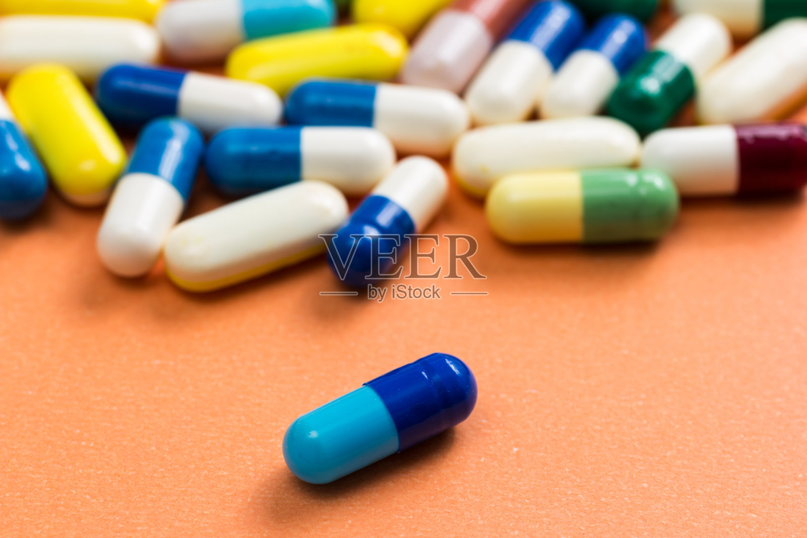 桔色背景上五颜六色的胶囊堆。一个蓝色的药丸是分开的，孤立的。照片摄影图片