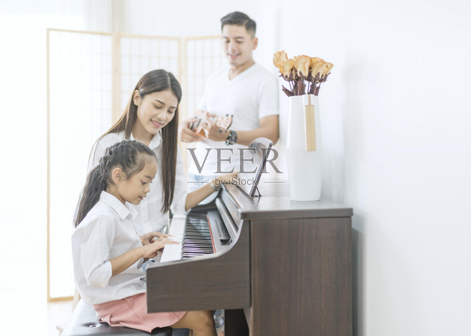 亚洲家庭，母亲和女儿弹钢琴，父亲在家里的家庭乐队演奏吉他，家庭关系的概念照片摄影图片