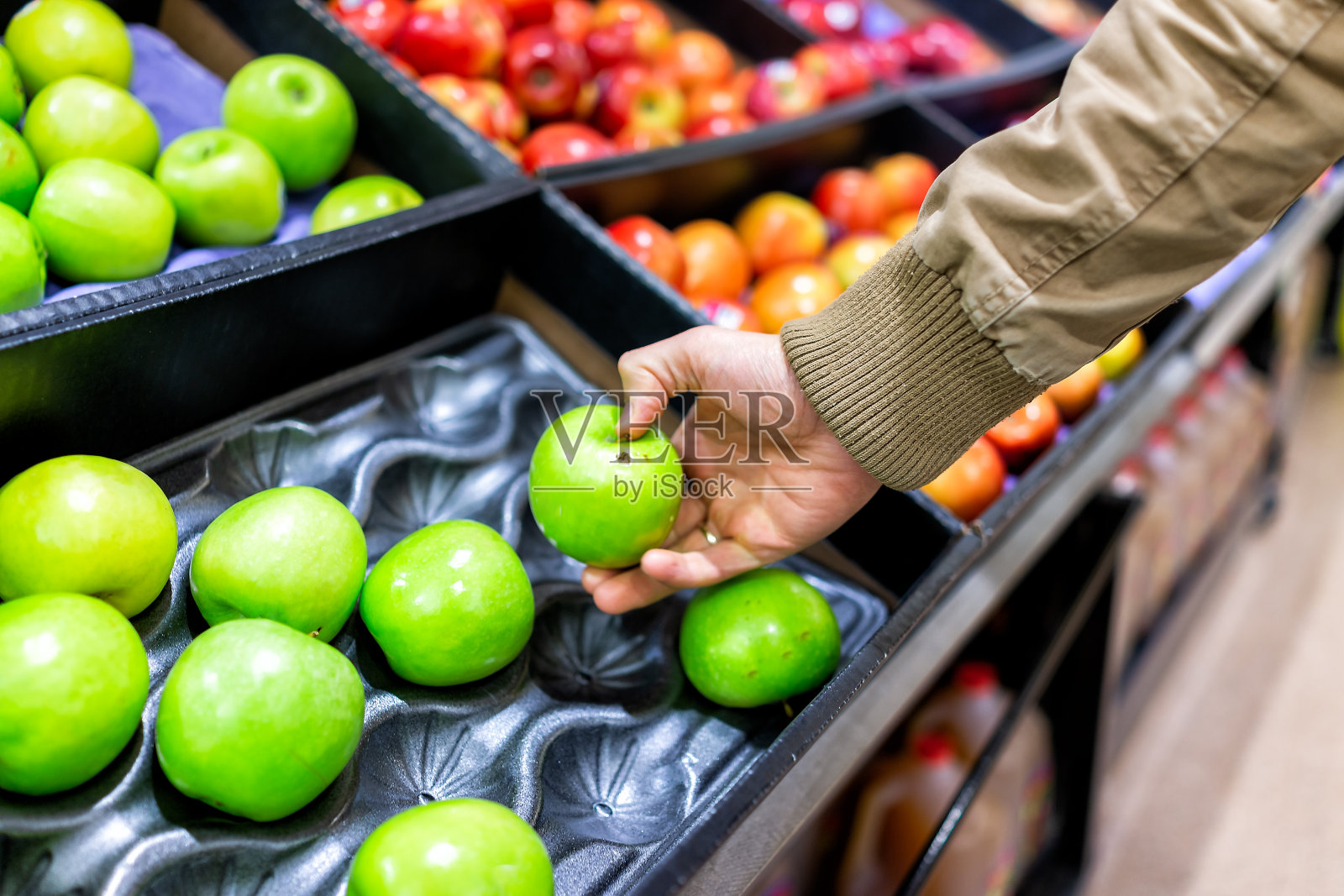 绿色的什锦苹果陈列在货架上的杂货店盒子里，超市里面，男人的顾客用手触摸绿果青照片摄影图片