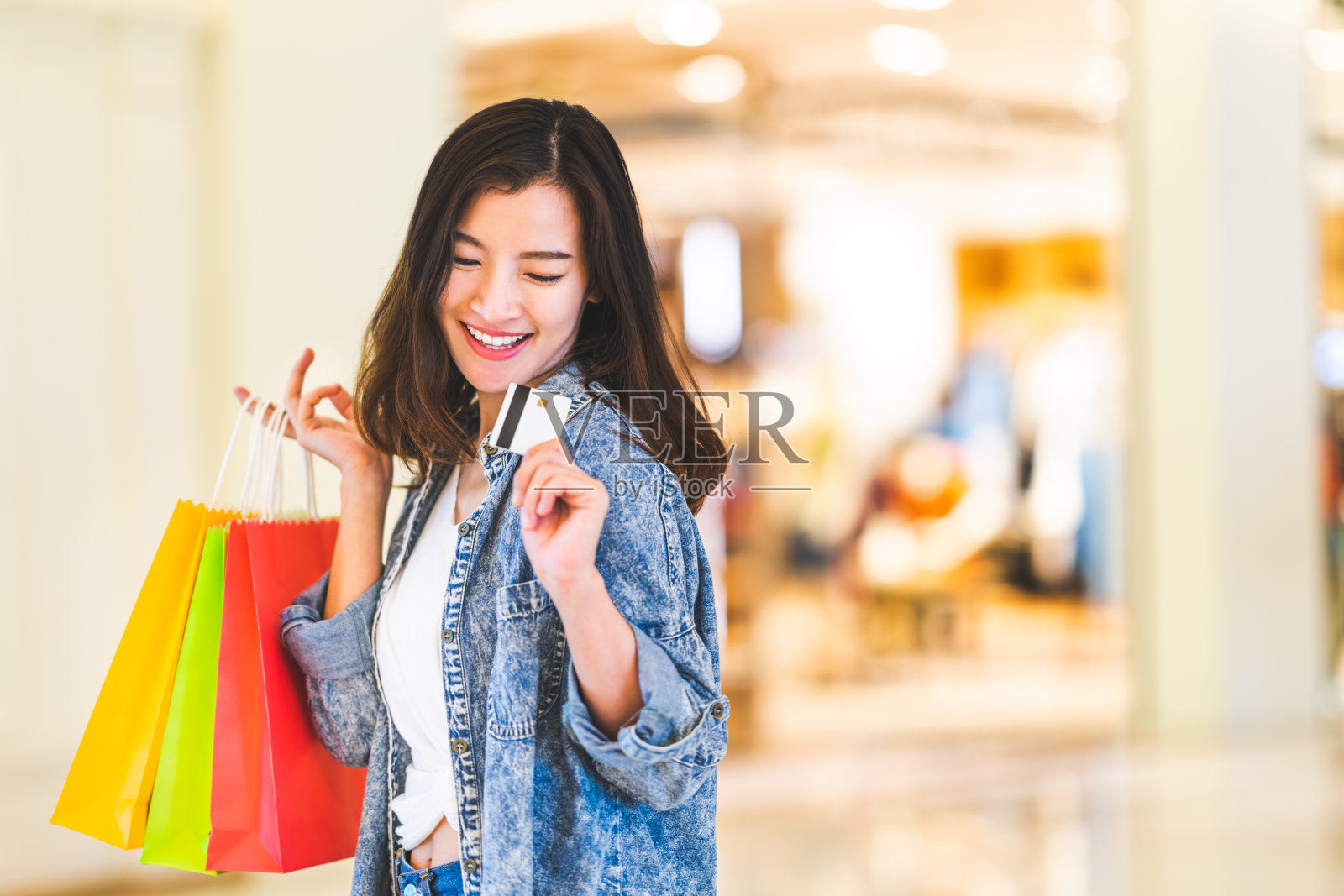 快乐美丽的亚洲女人微笑在信用卡，持有购物袋，复制空间在购物中心的背景。购物狂人，有钱的女孩花钱的生活方式，或百货公司的支付概念照片摄影图片