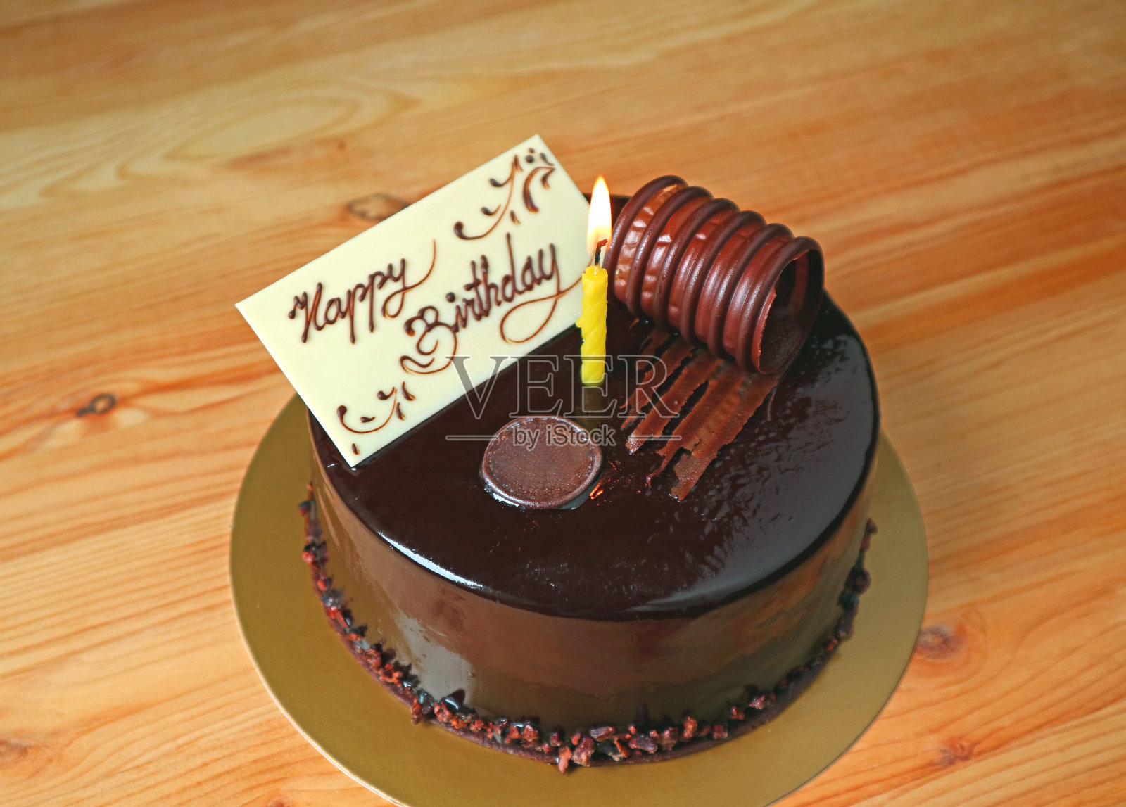 巧克力慕斯生日蛋糕顶部白巧克力贺卡和点燃蜡烛在木桌上照片摄影图片