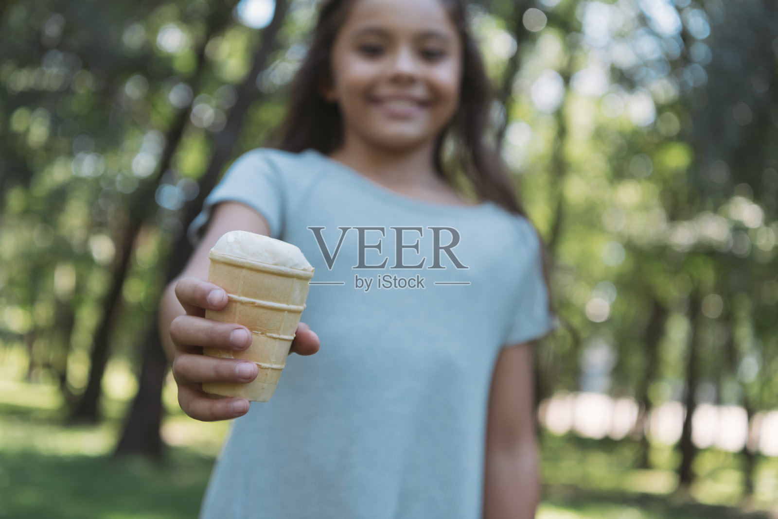 在公园里，一个可爱的孩子拿着冰淇淋对着镜头微笑照片摄影图片