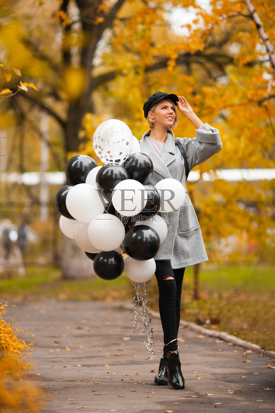 秋天的女人在秋天的公园里拿着气球。穿着灰色外套的时尚女孩照片摄影图片
