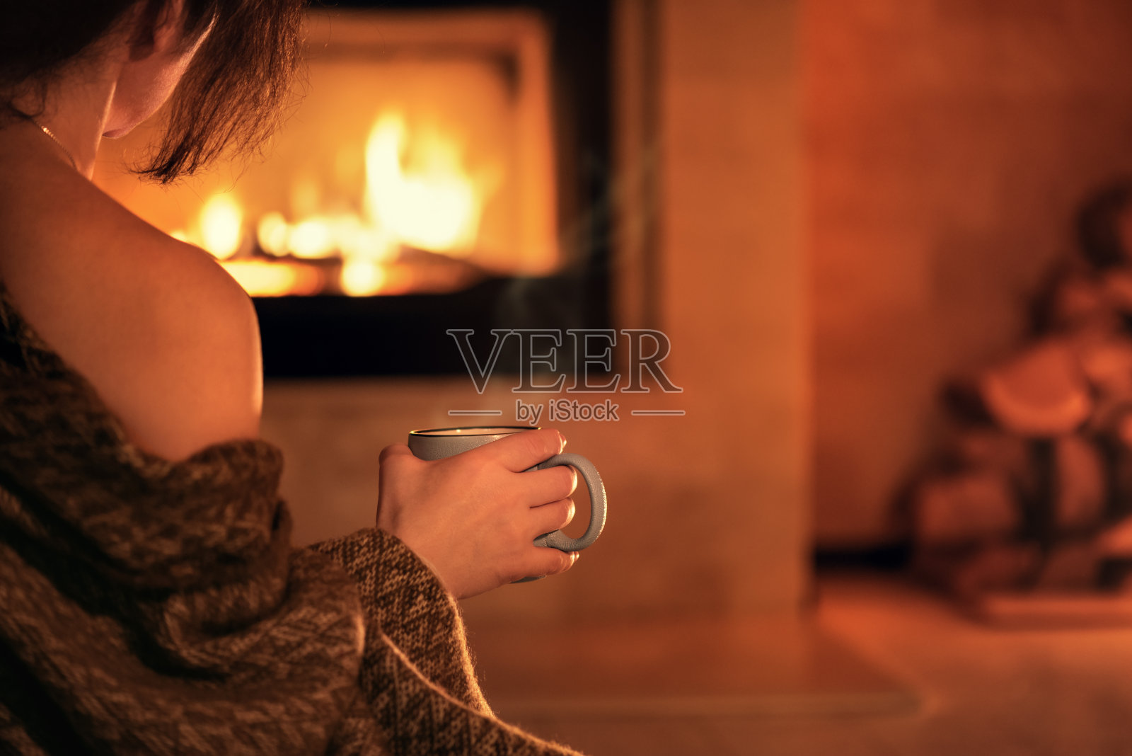 年轻女子坐在家里的壁炉旁喝着一杯热可可。照片摄影图片