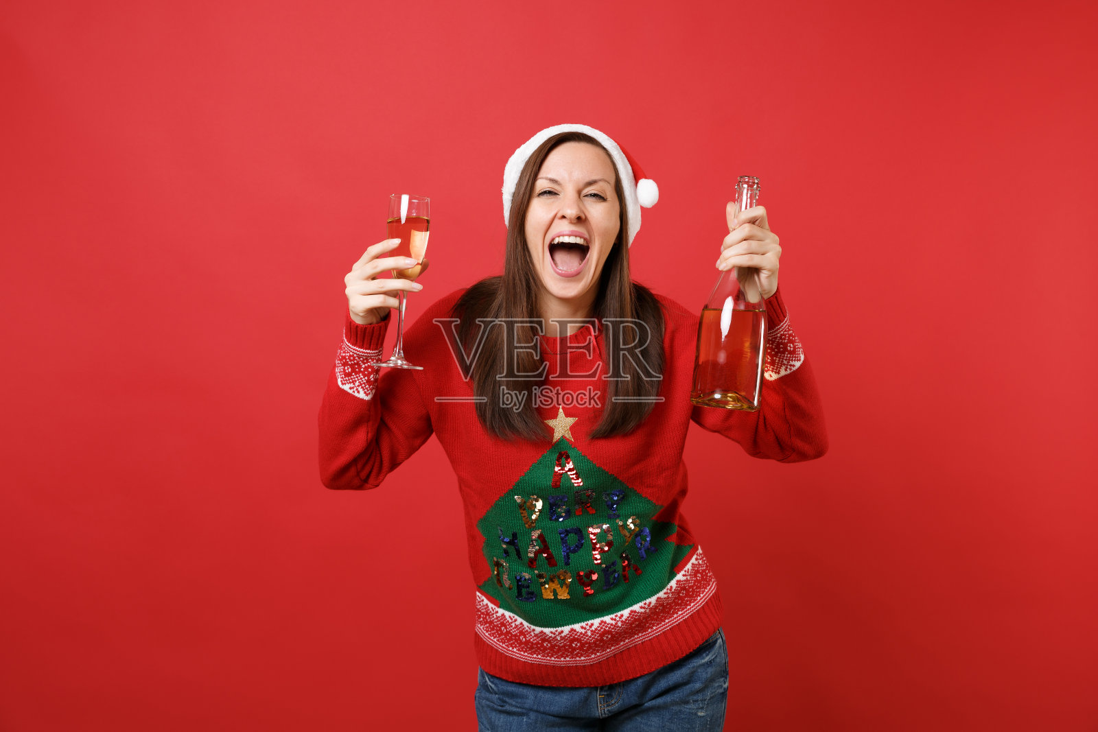 欣喜若狂的年轻的圣诞女孩在圣诞帽尖叫，拿着玻璃瓶的香槟孤立在明亮的红色背景。新年快乐2019庆祝节日派对概念。模拟拷贝空间。照片摄影图片