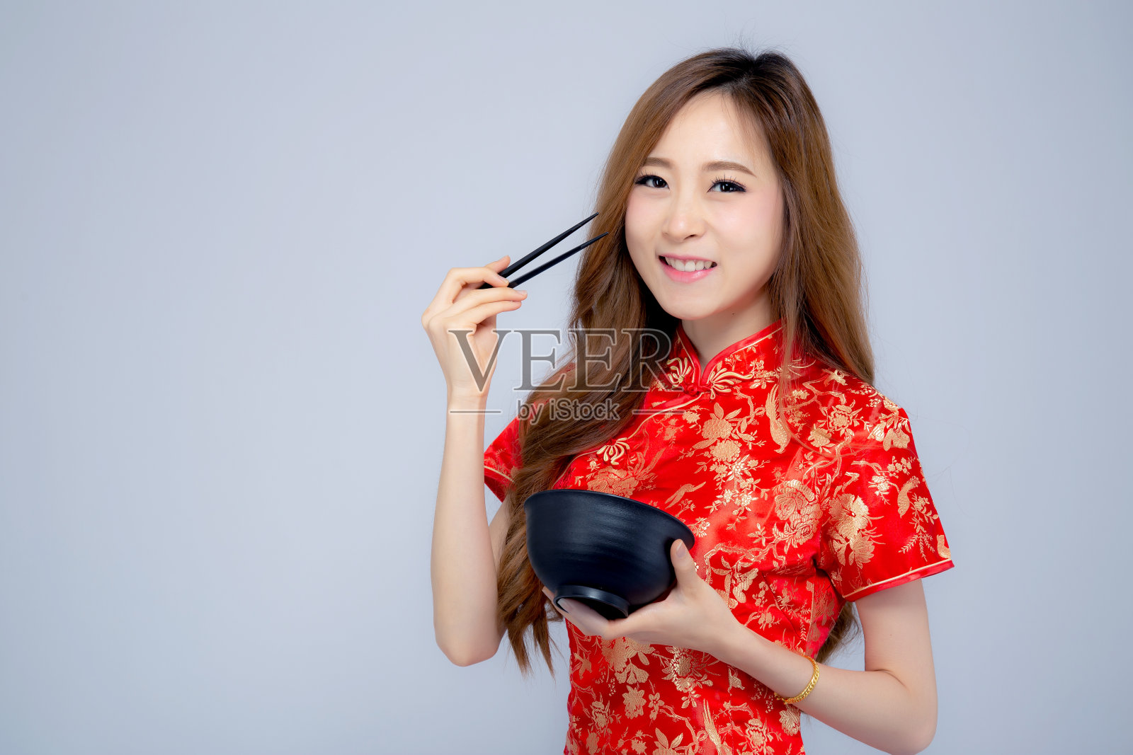 美丽的肖像年轻的亚洲妇女穿着红色旗袍拿着筷子和碗孤立在白色的背景，中国新年节日的概念。照片摄影图片