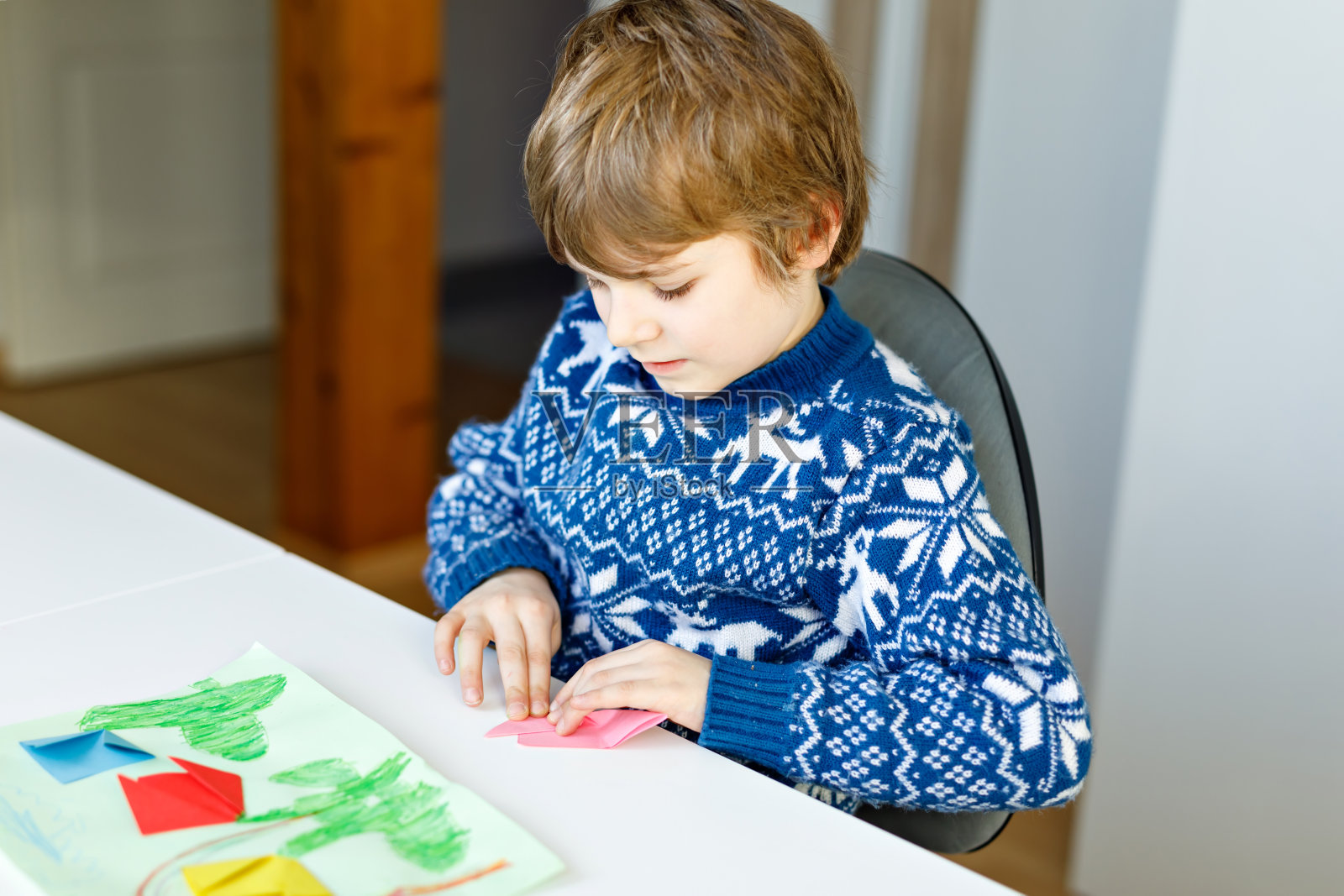 一个小男孩正在做折纸郁金香花作为母亲节或生日的明信片。小学可爱的孩子在做手工照片摄影图片