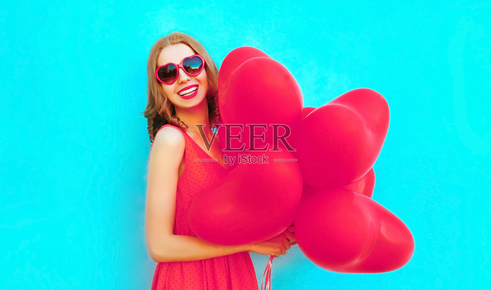 肖像快乐的笑年轻女子持有粉红色的心形气球在蓝色的背景照片摄影图片
