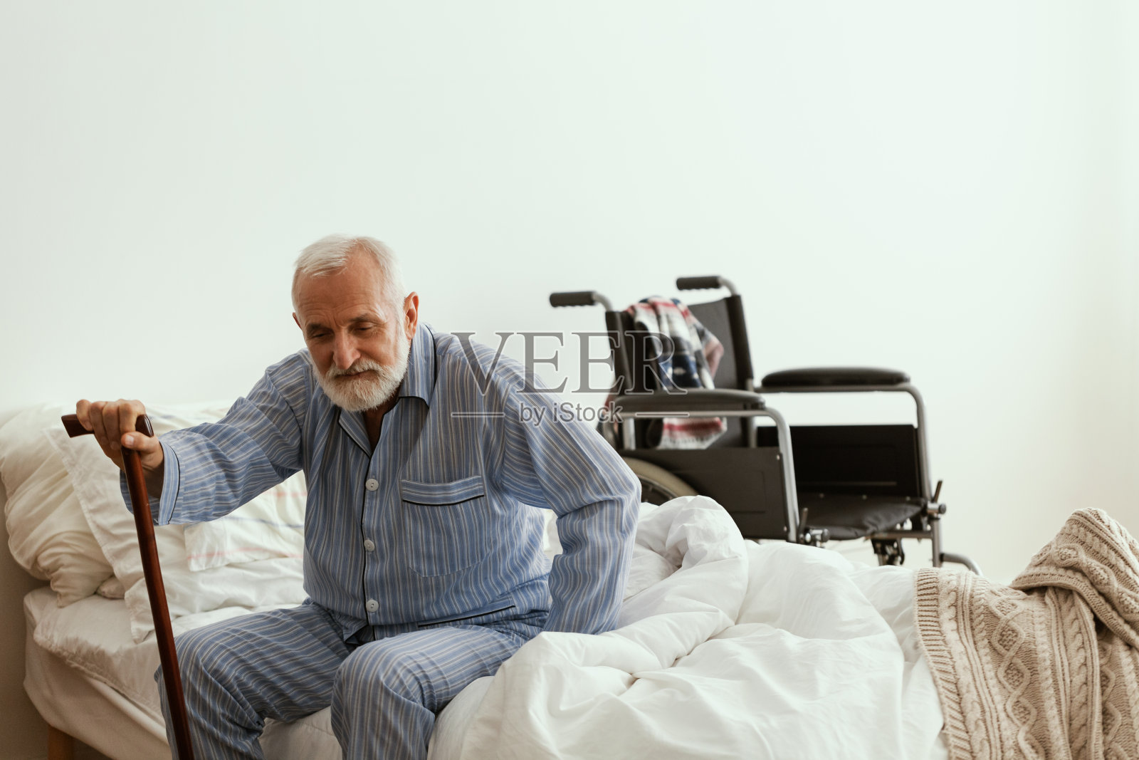 有灰色胡子和头发的老人穿着蓝色的睡衣坐在家里的床上照片摄影图片