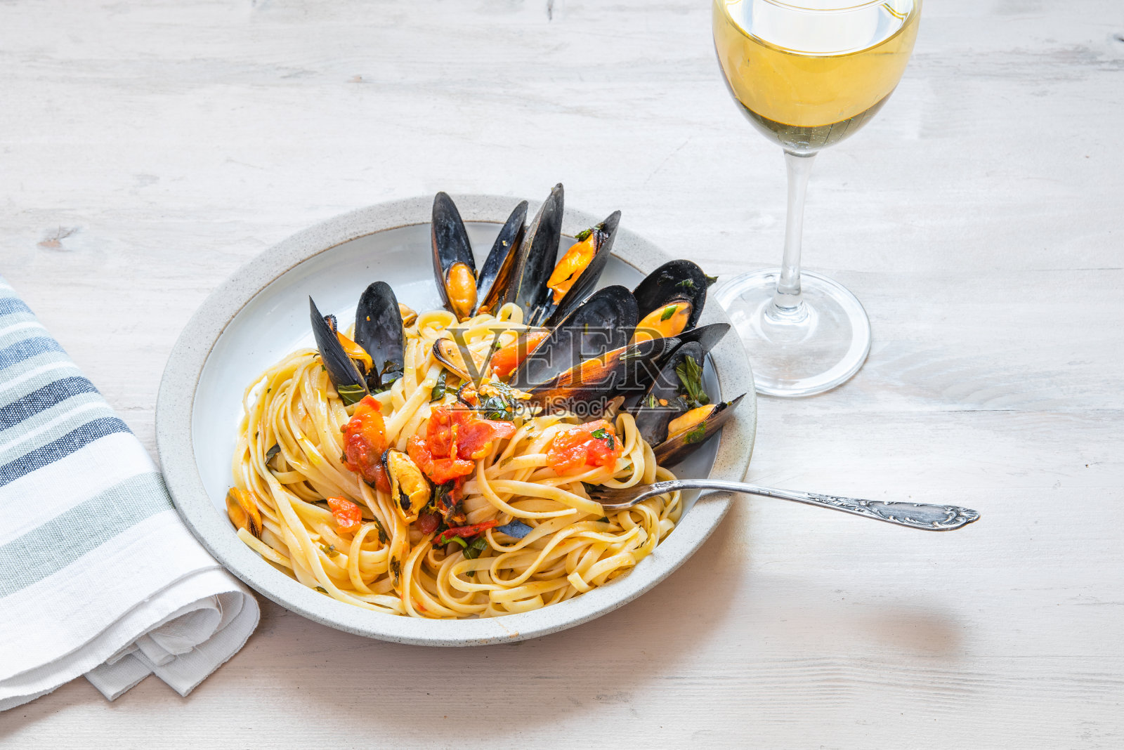 地中海午餐-扁意面与贻贝在一个盘子和一杯白葡萄酒在一个明亮的背景照片摄影图片