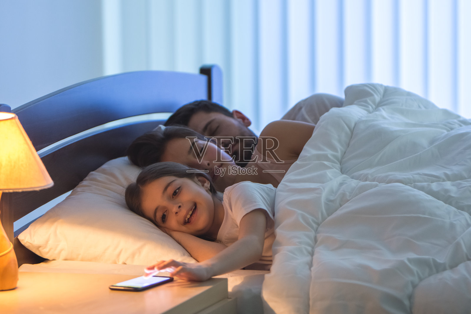 女孩在床上睡觉的父母旁边打电话照片摄影图片
