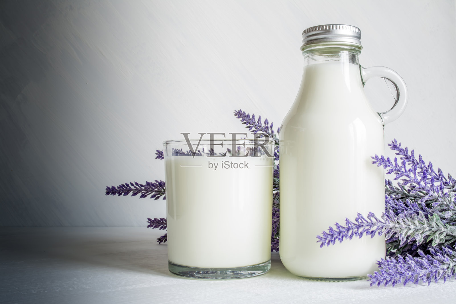一瓶牛奶，一杯牛奶和一枝薰衣草花在一个白色的复古背景照片摄影图片