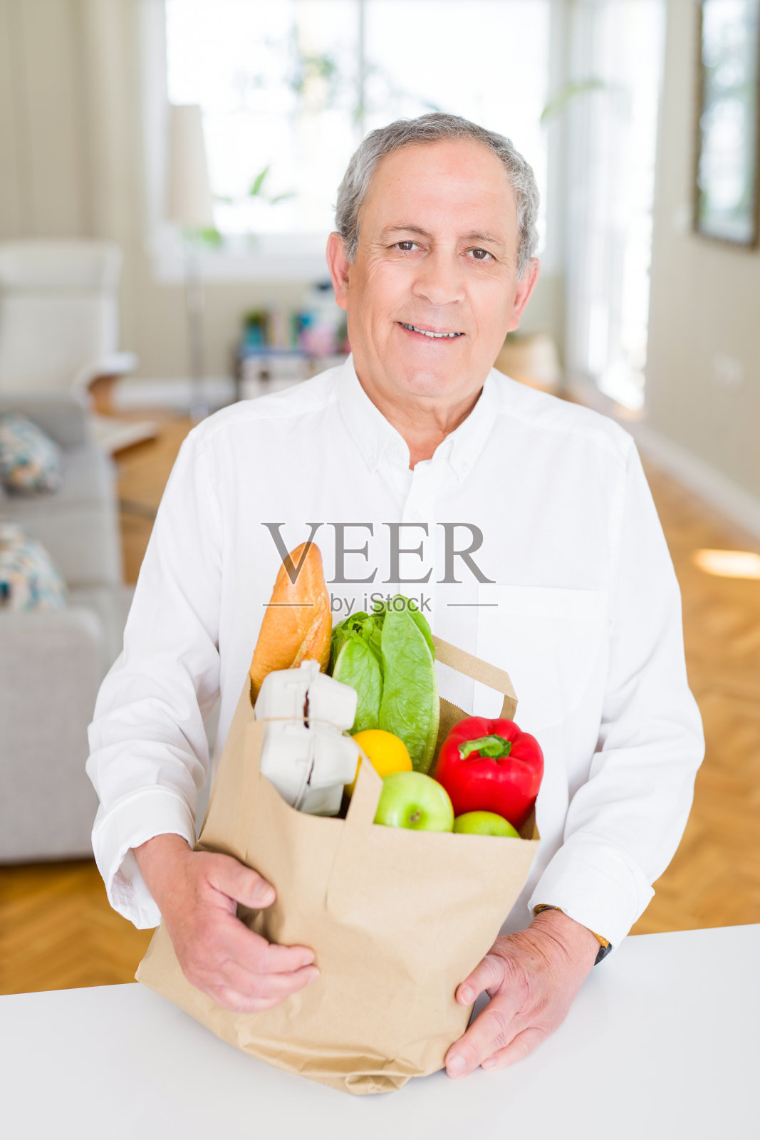 英俊的老男人拿着装满新鲜食品的纸袋，微笑着在家照片摄影图片