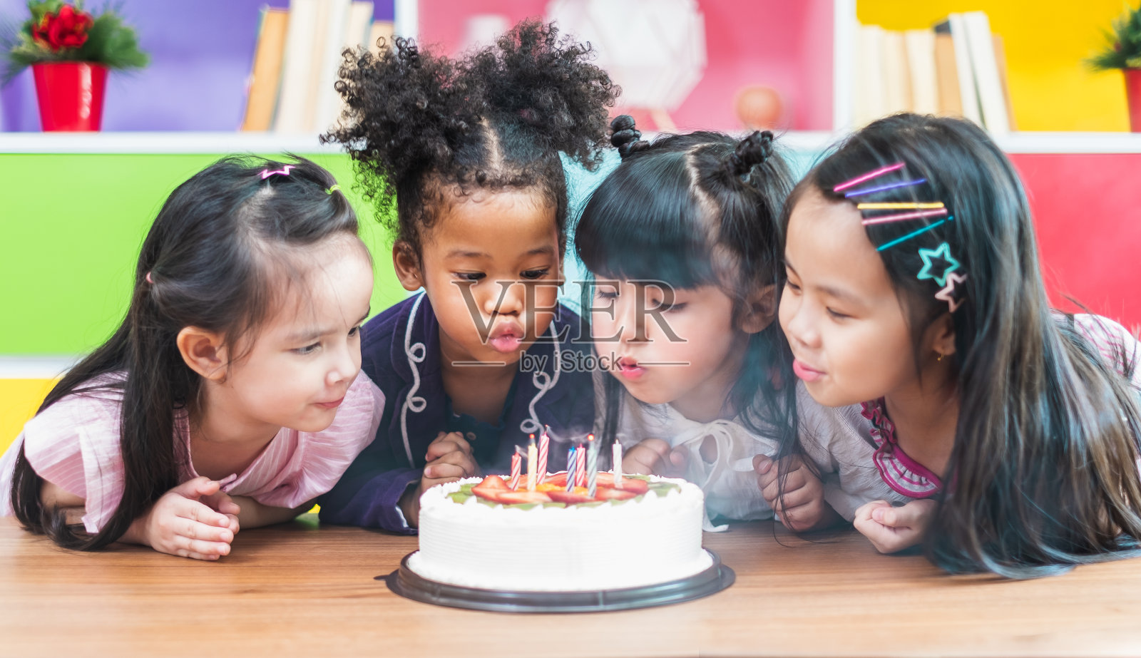 团体多元化的孩子吹生日蛋糕。照片摄影图片