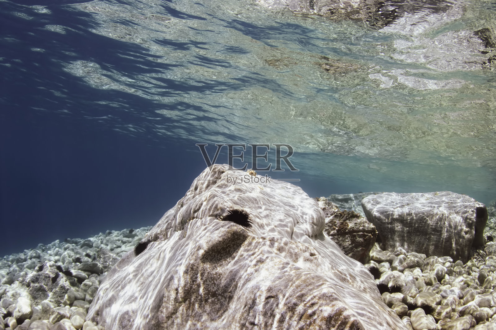 水下照片反射的岩石和清澈的蓝色浅海在希腊。照片摄影图片