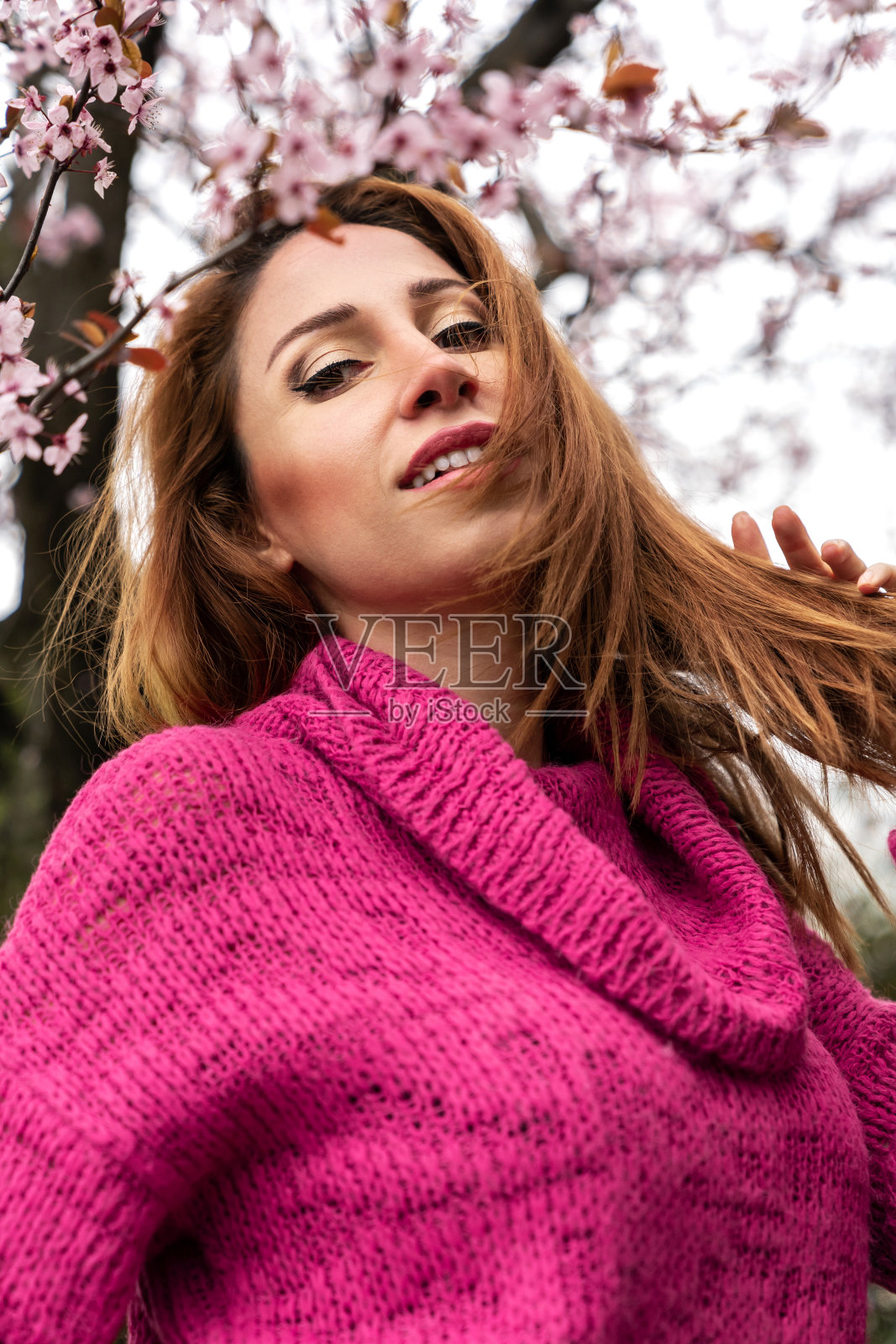 粉红花丛中的幸福女人，她有着闪闪发光的红头发照片摄影图片