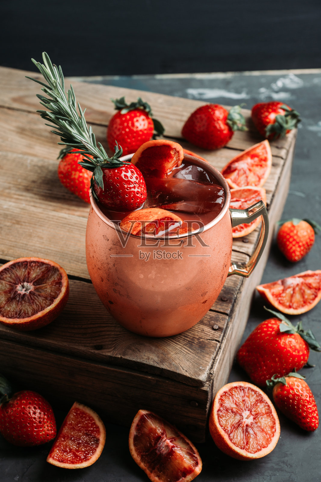 红橘子和草莓鸡尾酒铜杯(变种莫斯科骡子)在木制背景照片摄影图片