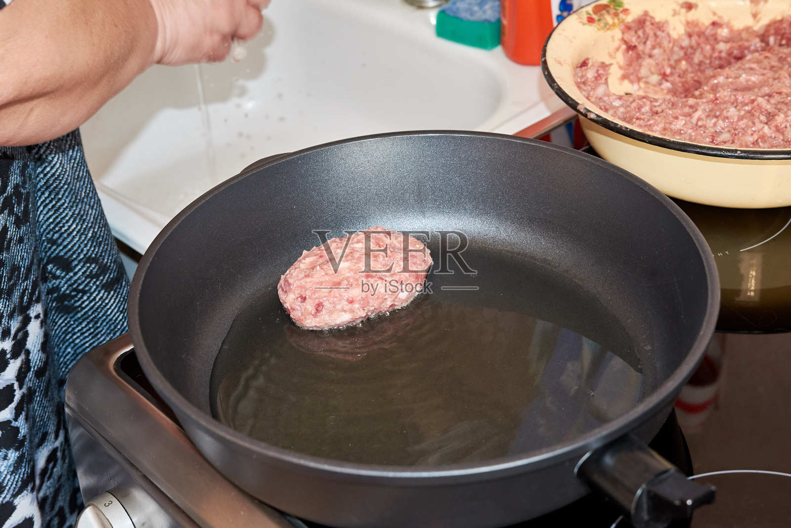 一名妇女在家的厨房里，用电炉上的热煎锅煎猪肉和牛肉片照片摄影图片
