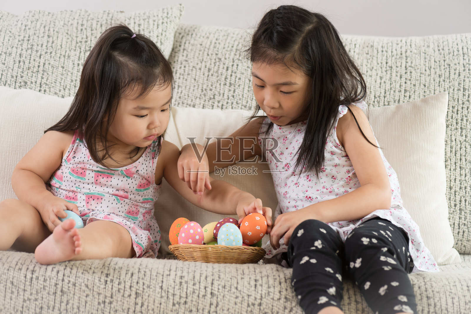复活节快乐!两个可爱的小孩坐在沙发上，他们的窝里或篮子里放着复活节彩蛋。照片摄影图片